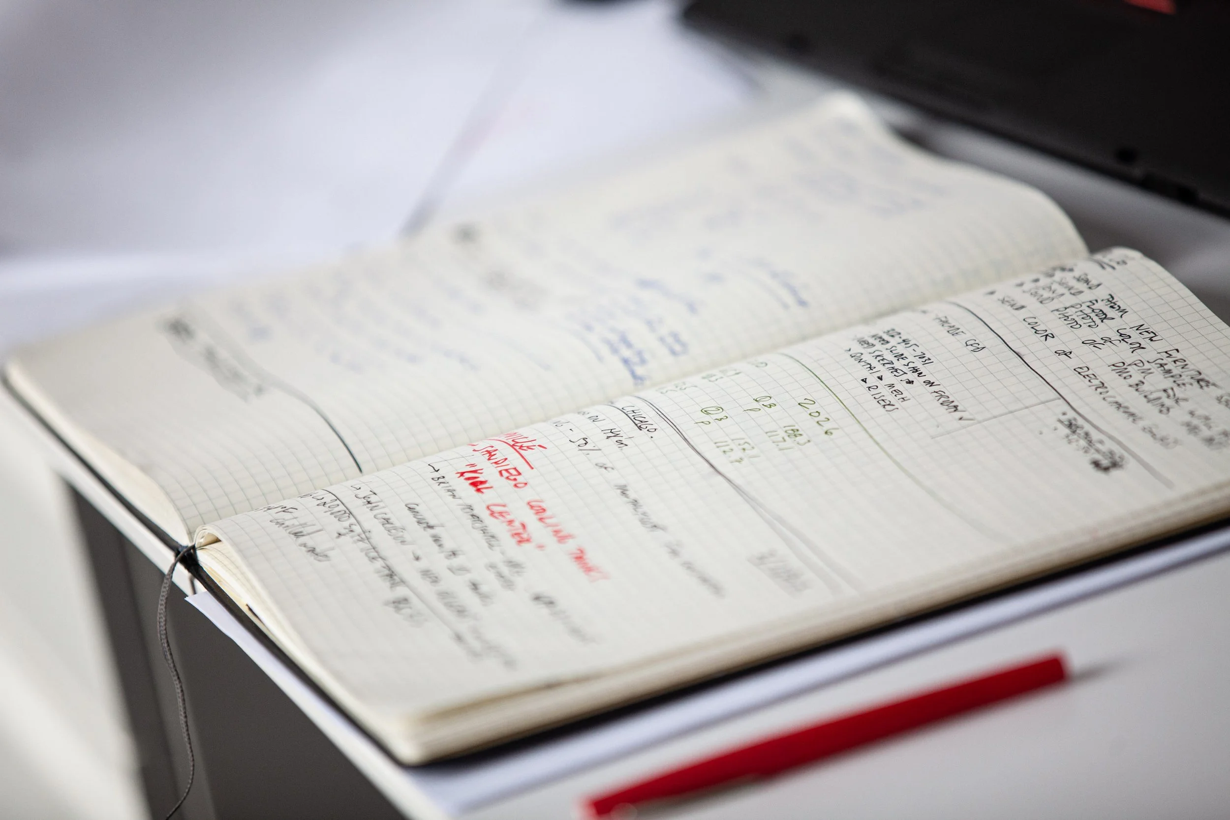 Open notebook with handwritten notes, resting on a desk, with a blurred background.