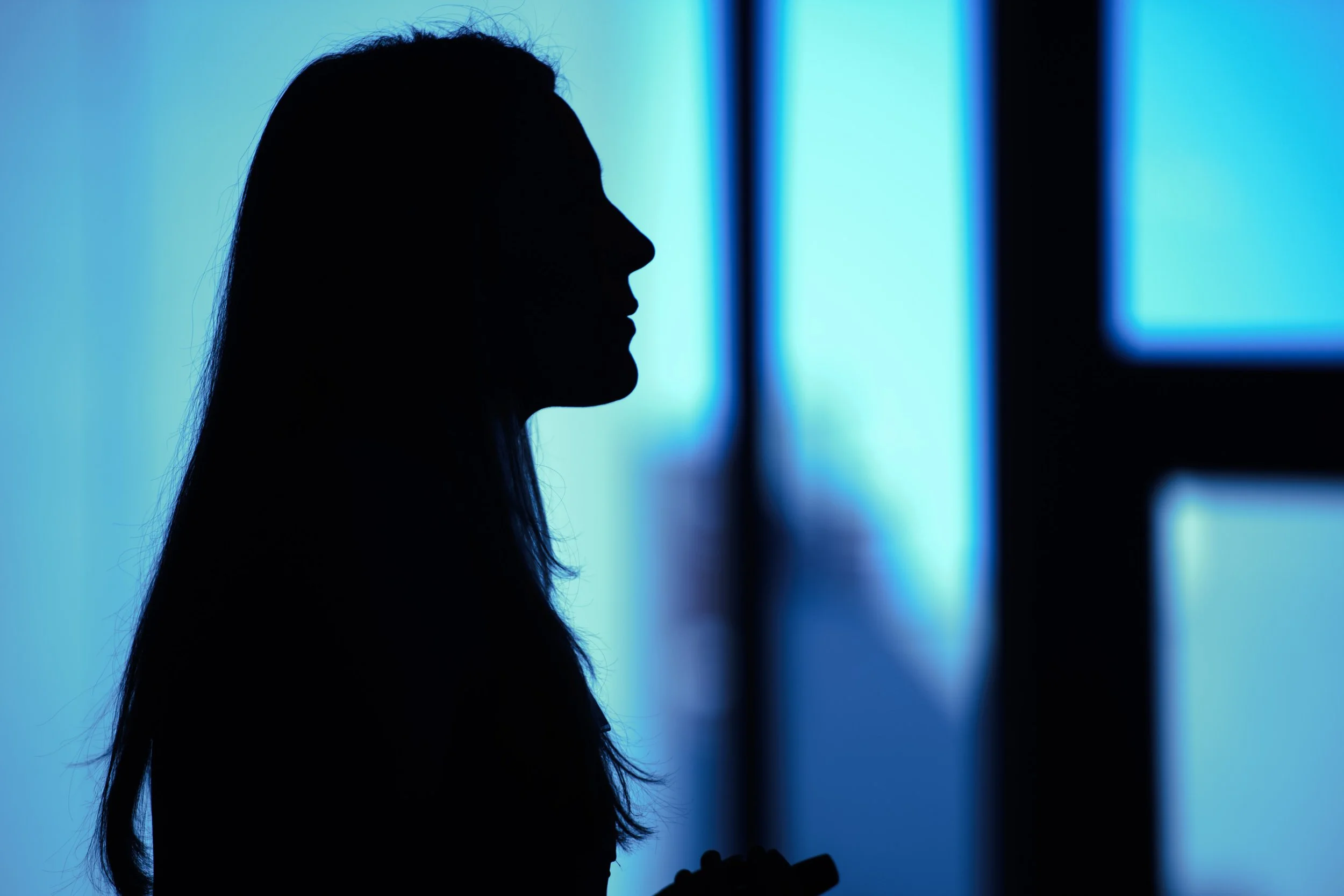 Silhouette of a woman with long hair, facing left, in front of a blue-lit background.