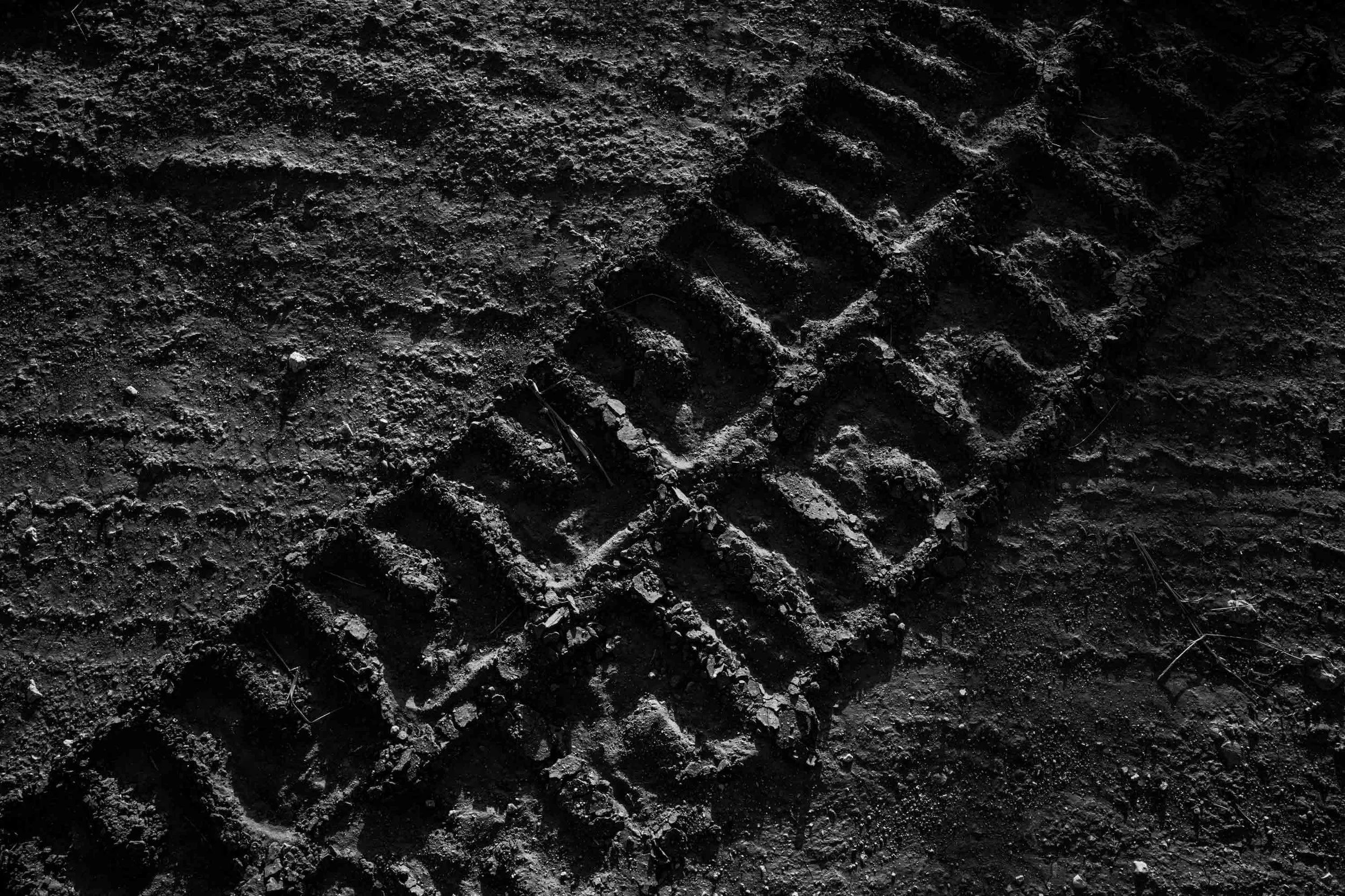 Dark, textured soil with tire tracks and footprints.