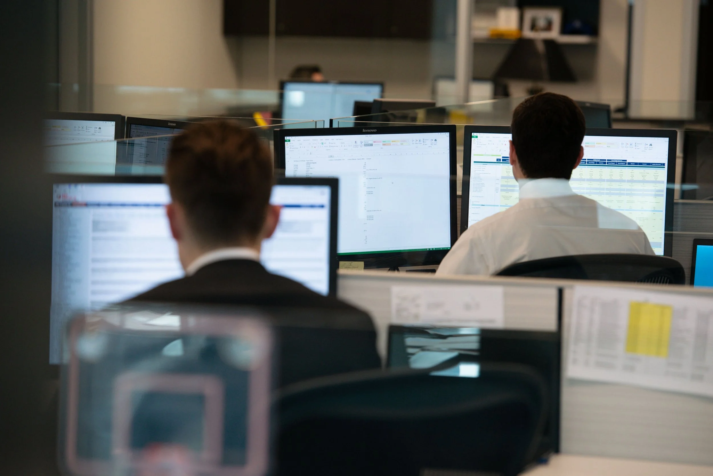 Employees working at computers in an office with a glass partition.
