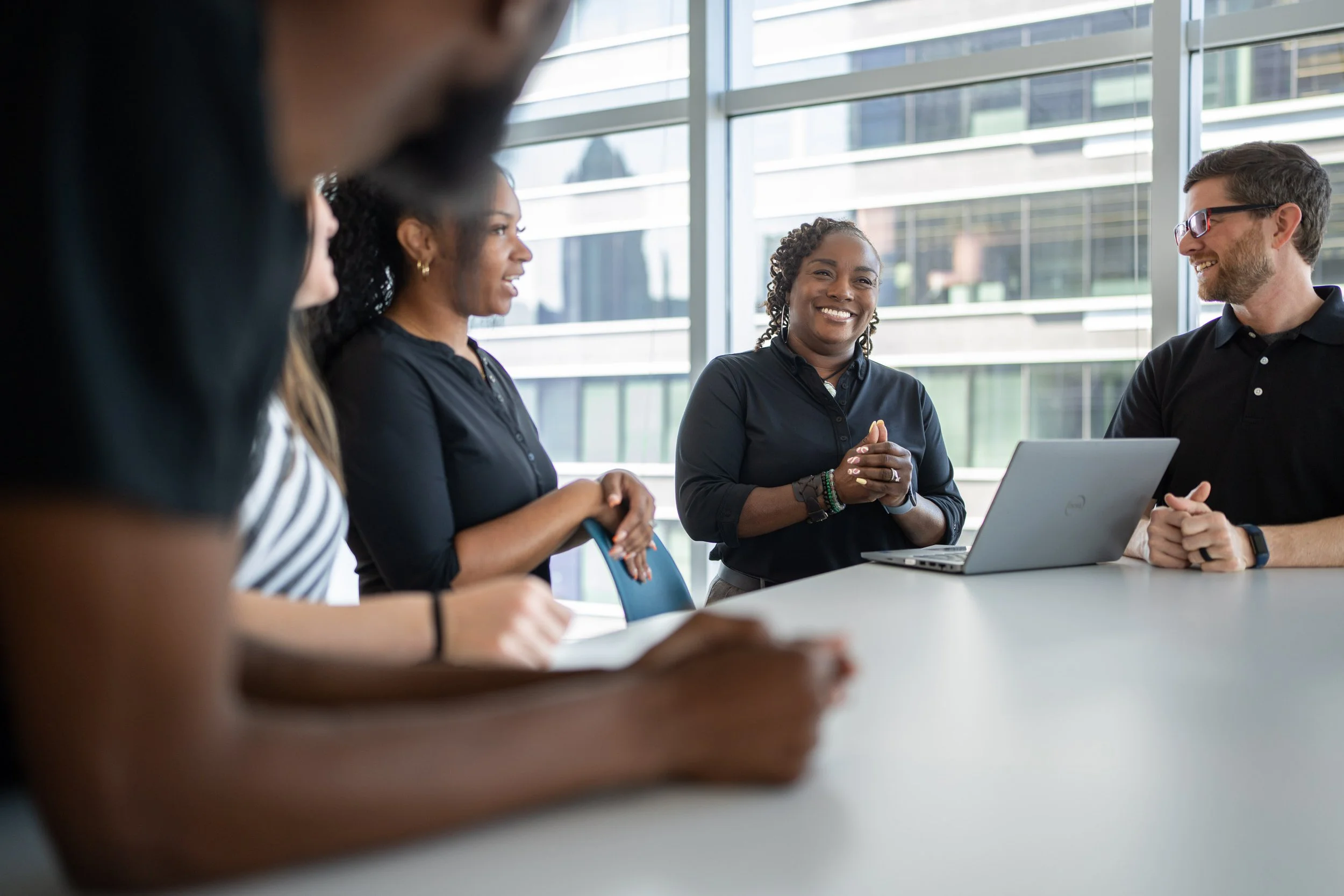 Group of diverse professionals engaging in a meeting in a modern office with large windows.