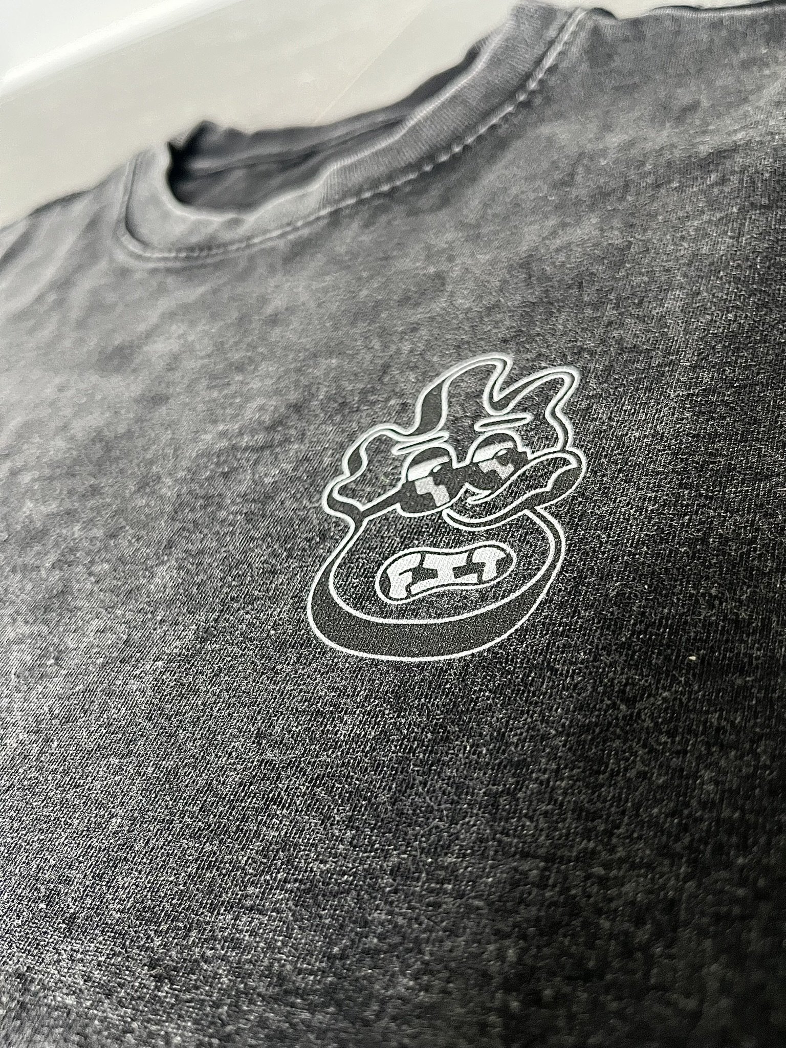 Close-up of a black fabric shirt with a white embroidered cartoonish face and eyes, visible next to a partial zippered collar.