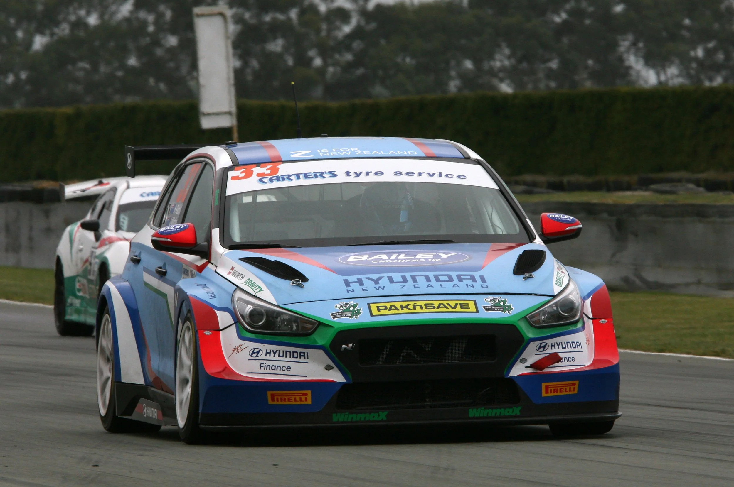 Colorful Hyundai race cars on a track during a race, with sponsor logos and racing numbers visible.