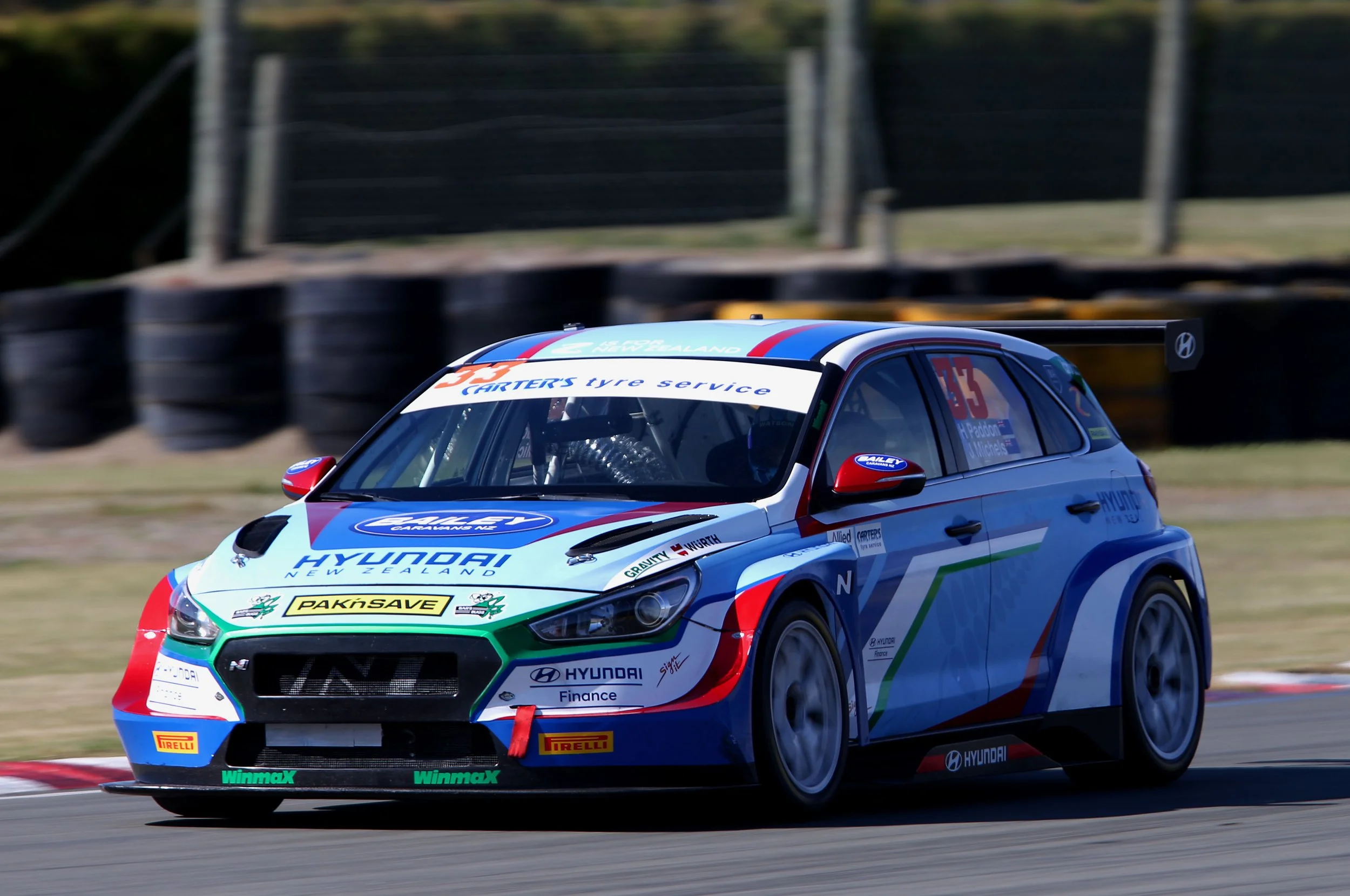 A rally car decorated with Hyundai and sponsorship logos racing on a track.