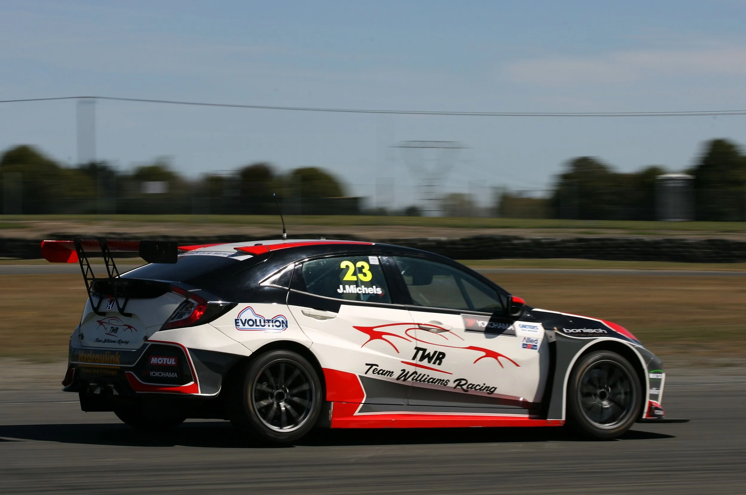 A race car speeding on a track with a blurred background of trees and power lines, number 23, sponsored by Team Williams Racing.