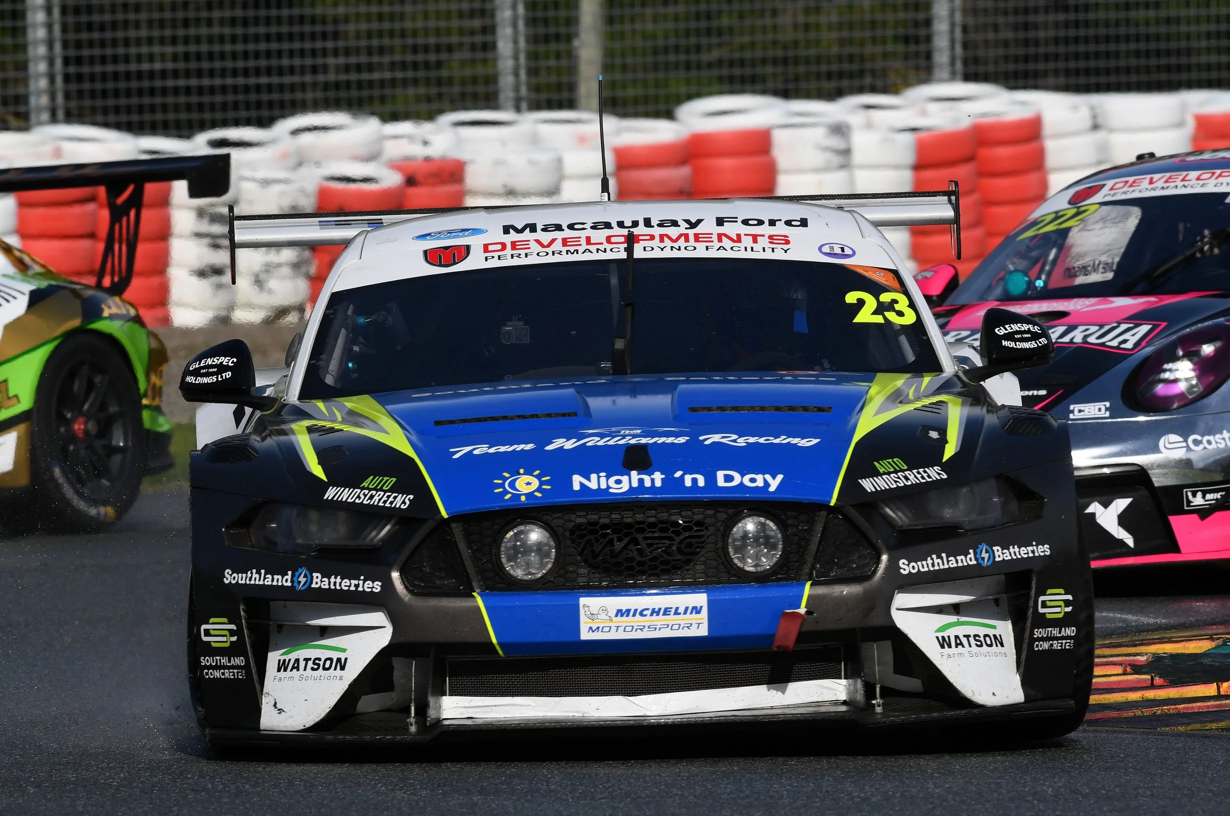 Close-up of race cars on a track during a motorsport event, with tire barriers in the background.