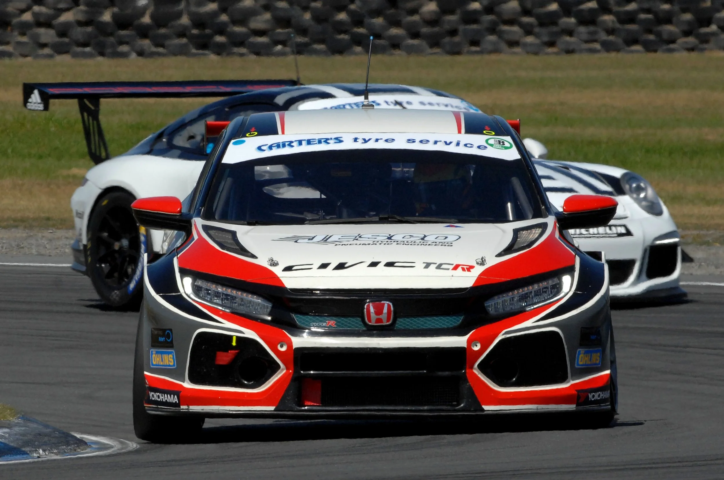 Close-up of a racing car on a track, with other race cars behind it, while racing on a curved section of the track.