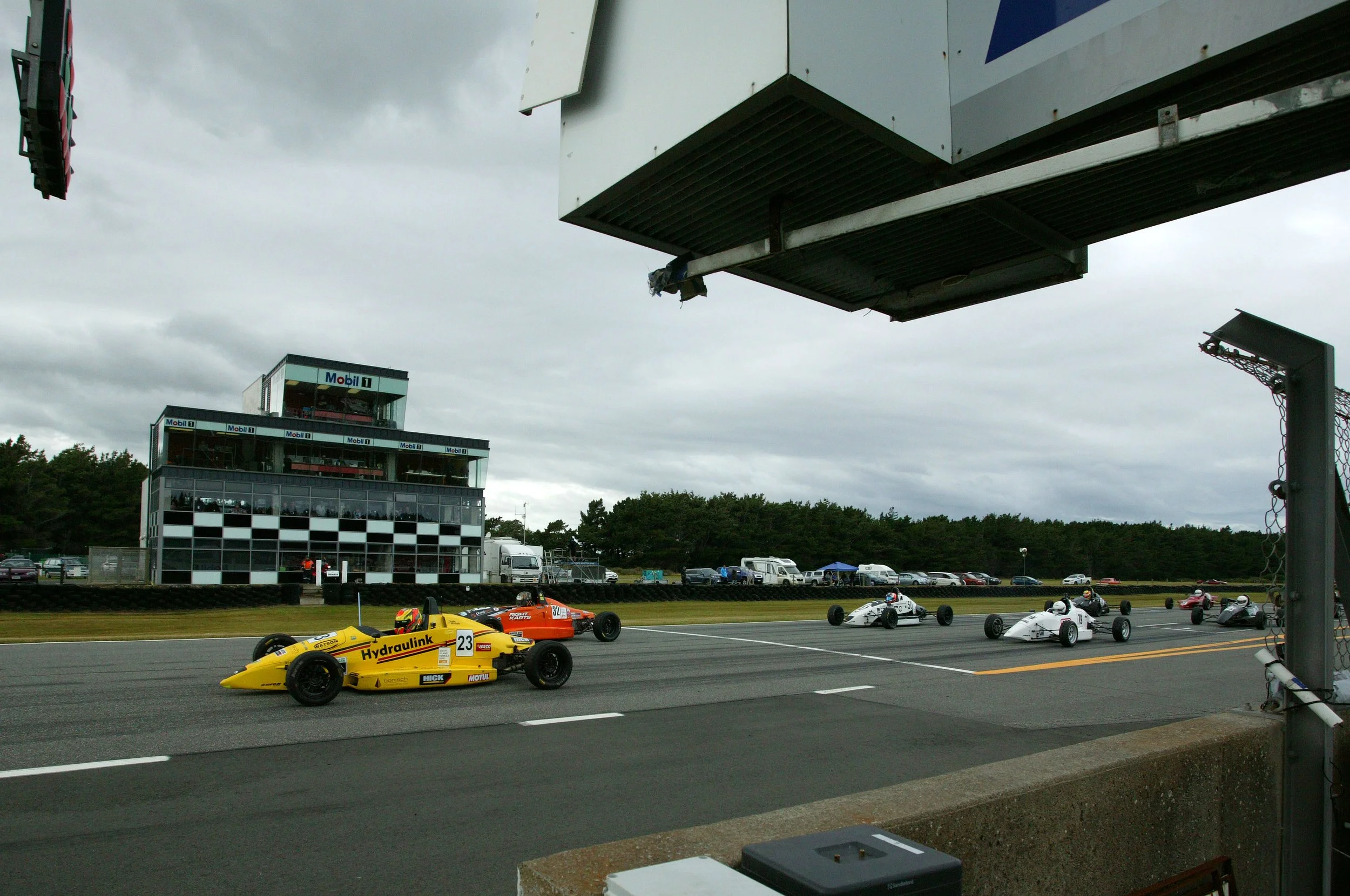 Race cars on a race track with a building in the background and an overcast sky.
