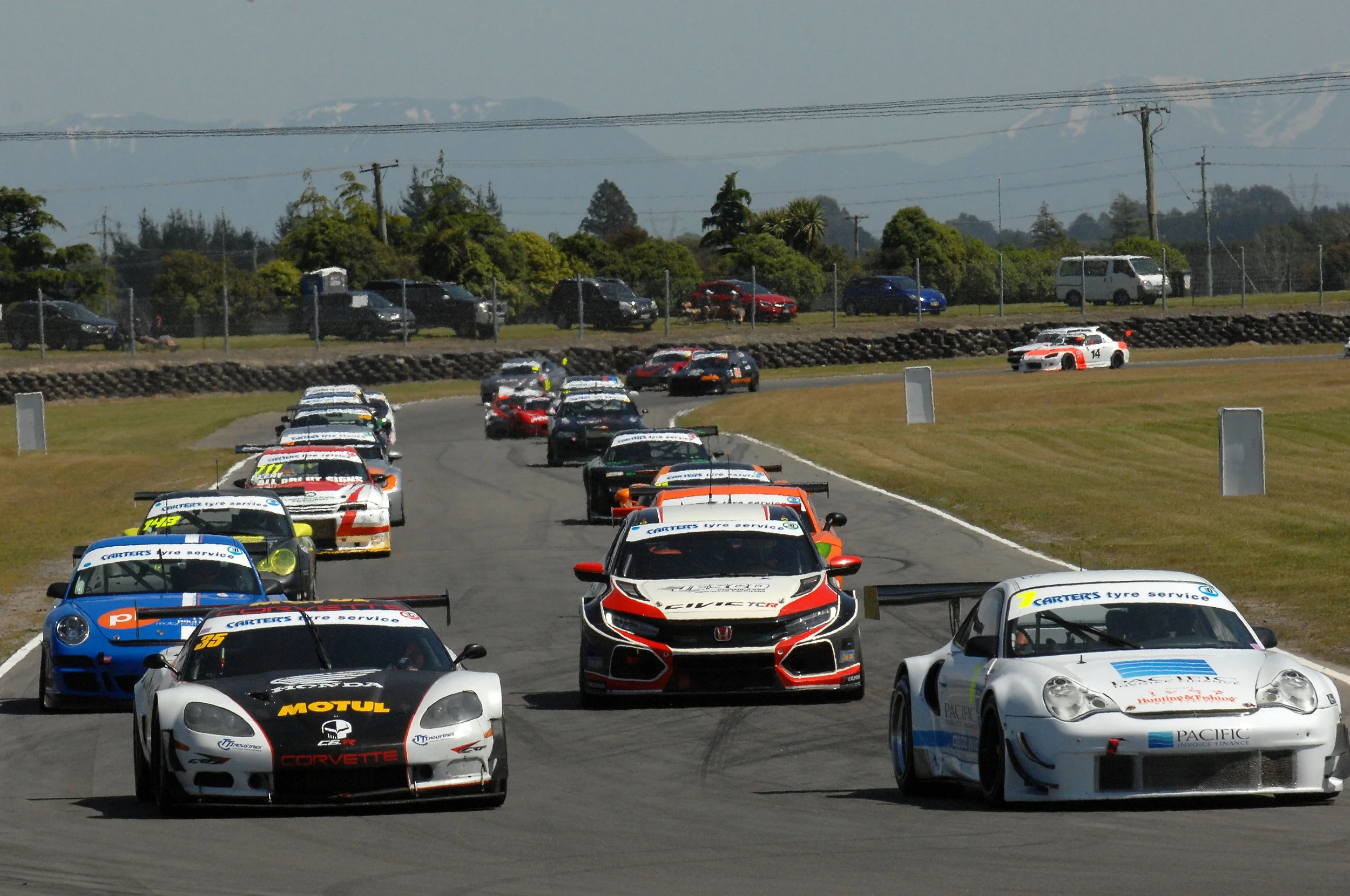 A group of race cars driving on a race track, with some cars ahead and others in the background, racing during a motorsport event.