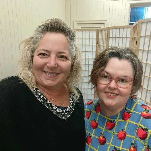 Two women, owners of HBOT NZ in Timaru, smile at the camera, standing in the HBOT NZ clinic which is cream and calm