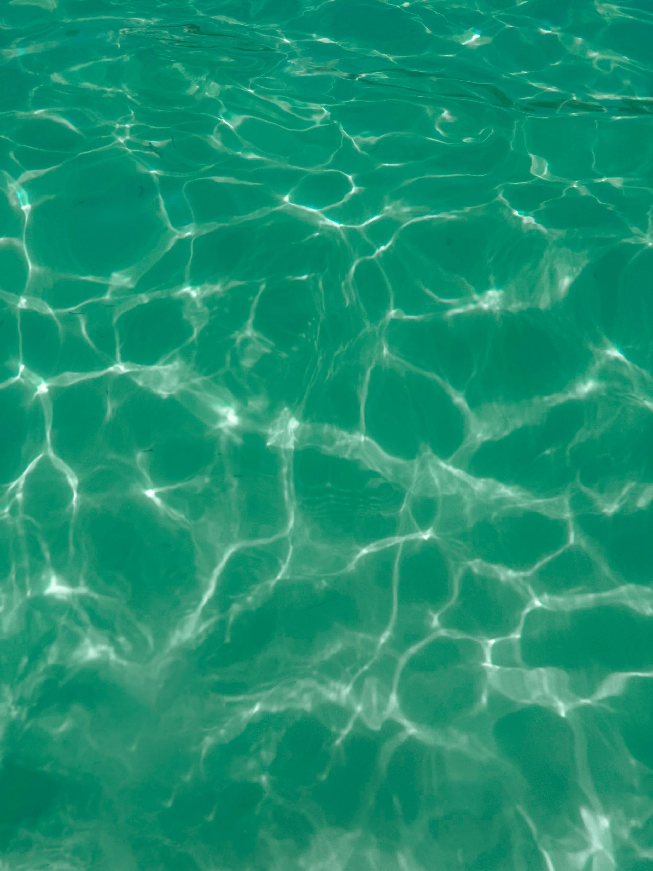 Clear turquoise water with sunlight reflections creating a pattern on the surface.