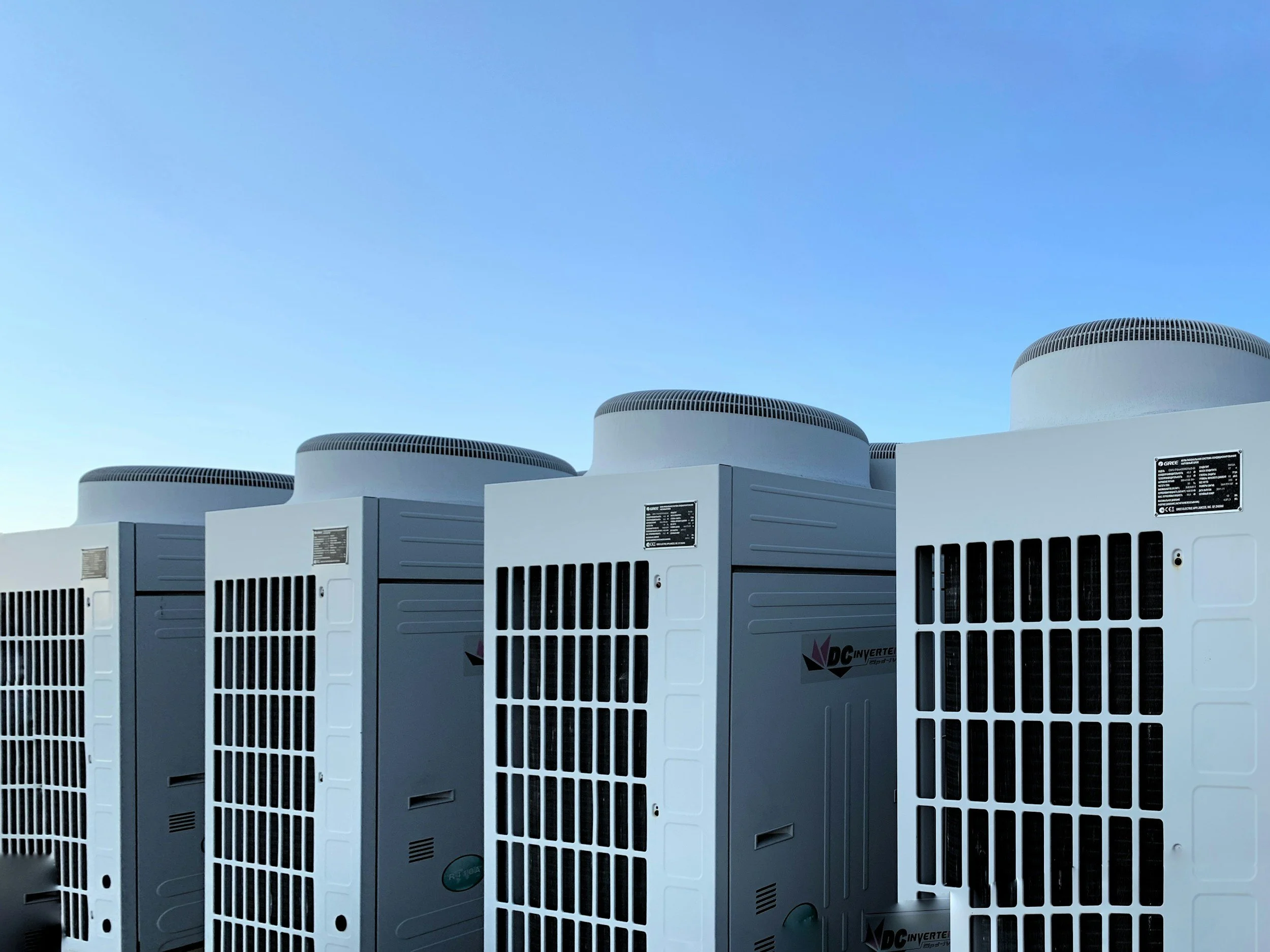 Multiple white industrial air conditioning units with black vents on top, set against a clear blue sky.
