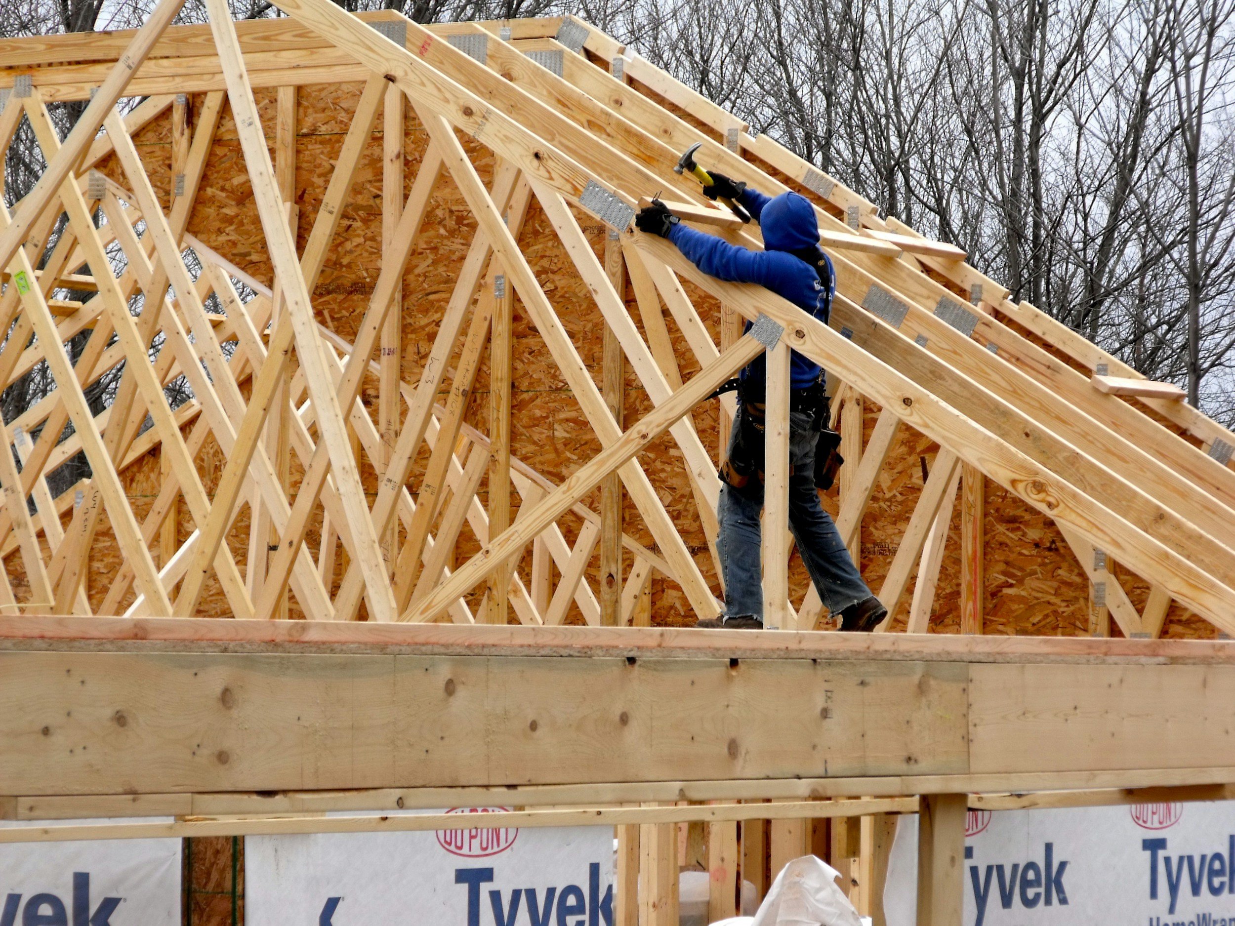 Construction worker installing roof rafters on a wooden building frame.