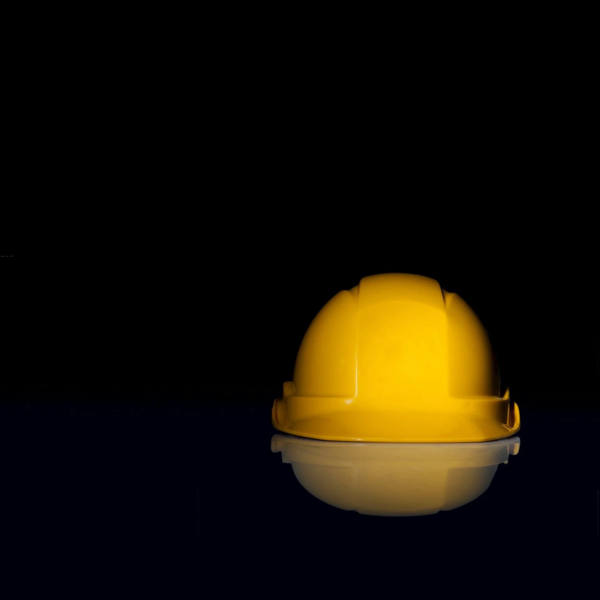 Yellow construction helmet placed upside down on black surface with reflection, isolated on black background.