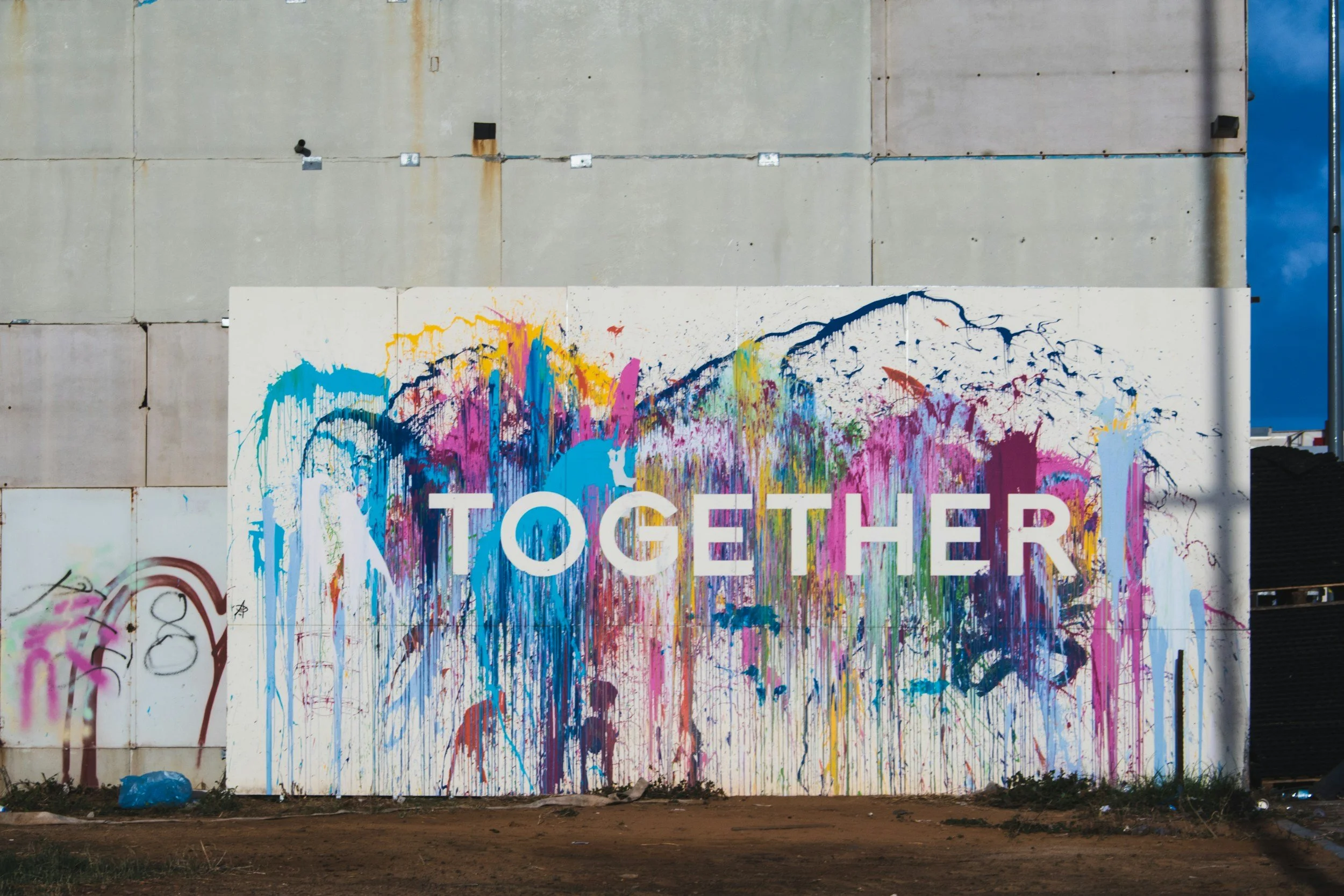 A graffiti mural on a wall with the words "TOGETHER" written in large, colorful letters, surrounded by vibrant paint splatters and abstract designs.