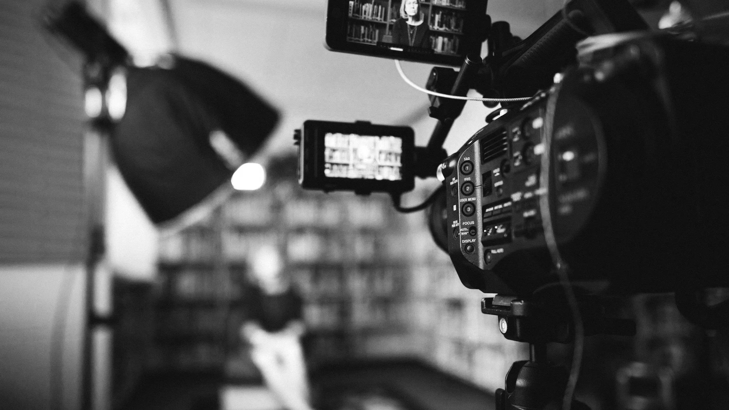 Black and white photo of a video camera filming a woman in front of a bookshelf.