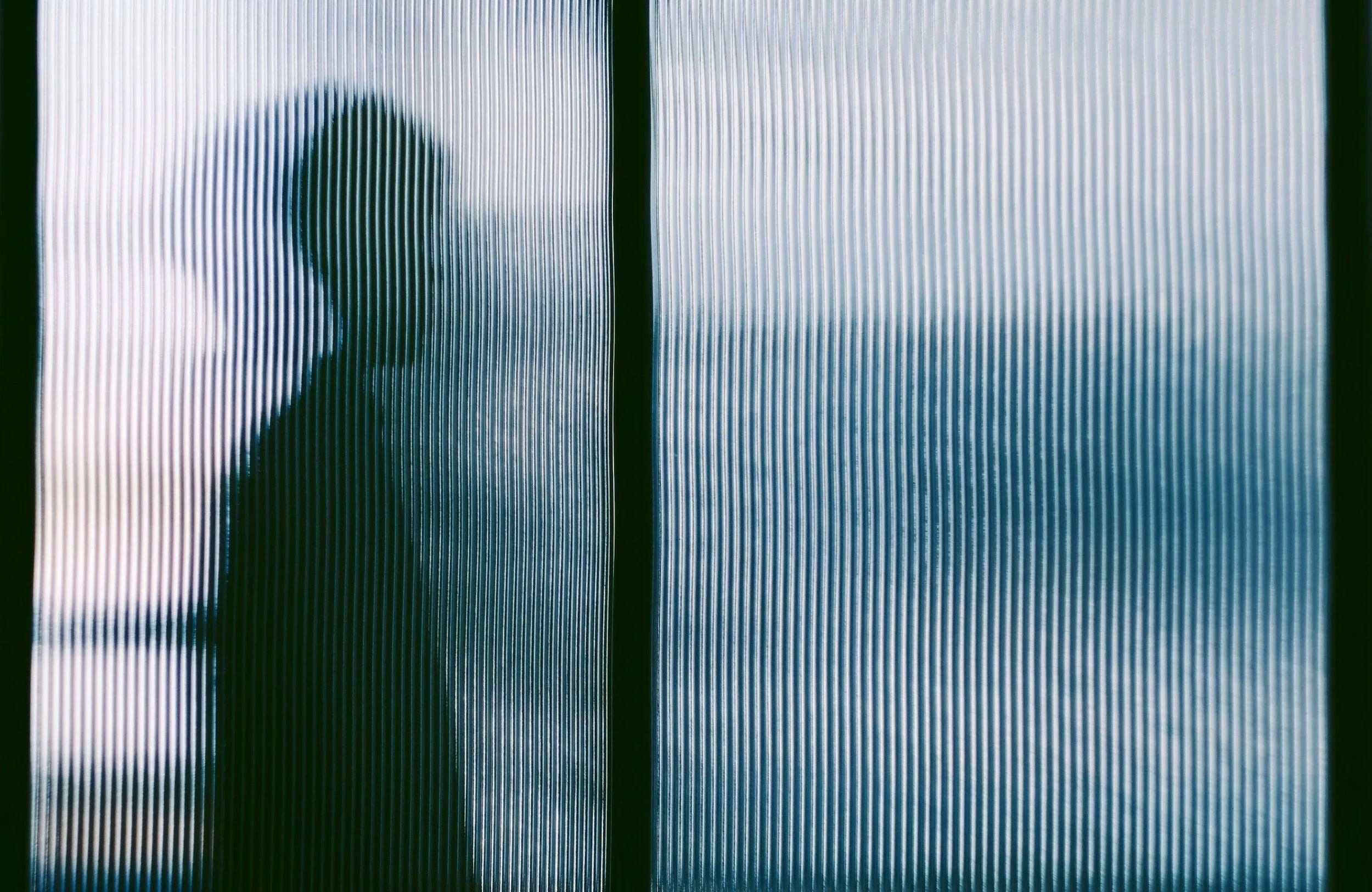 Abstract textured glass with a blurred dark silhouette of a person's profile behind it.