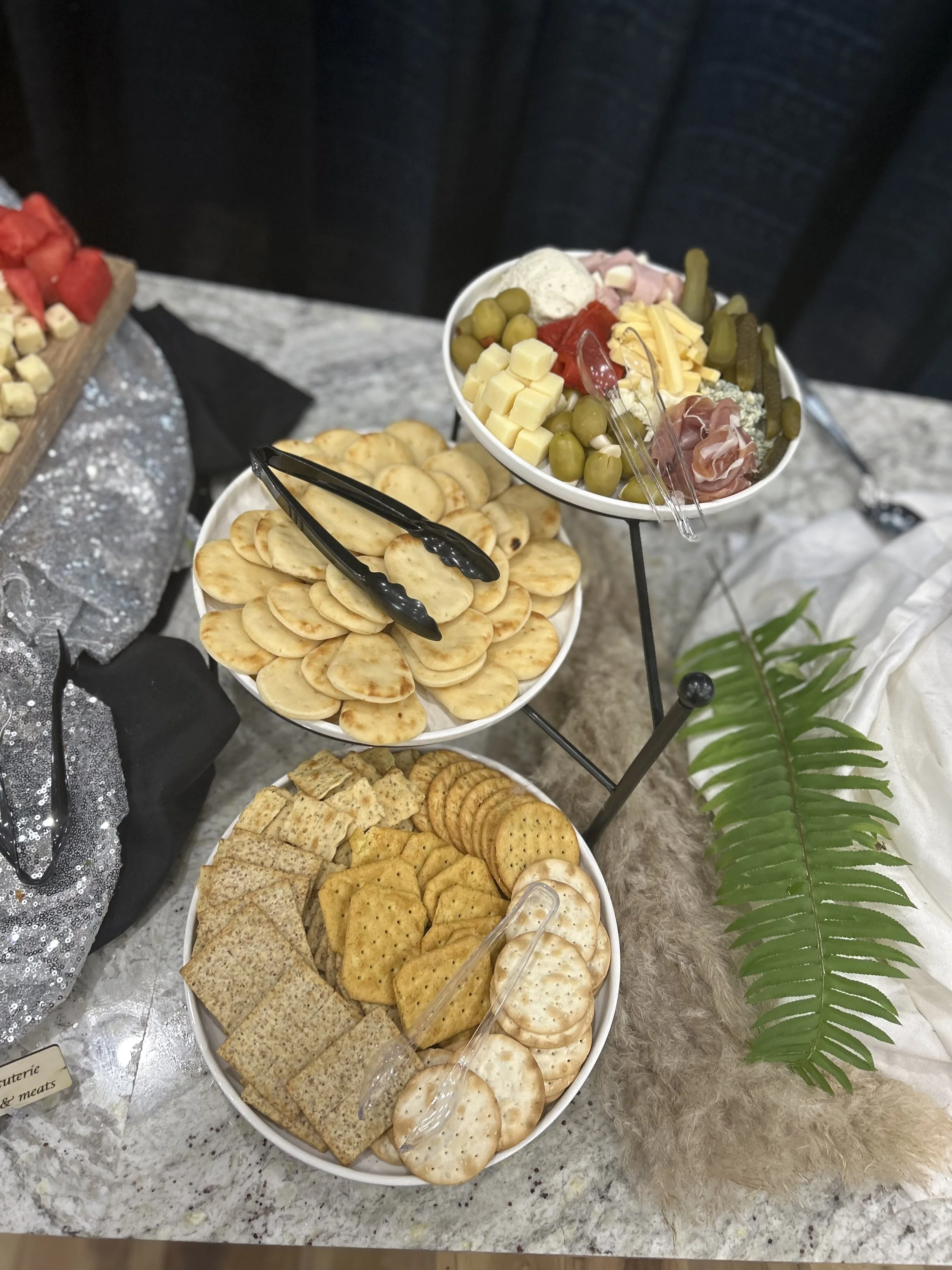 A platter of assorted crackers and sliced cheeses on a marble table, with some greenery and decorations nearby.