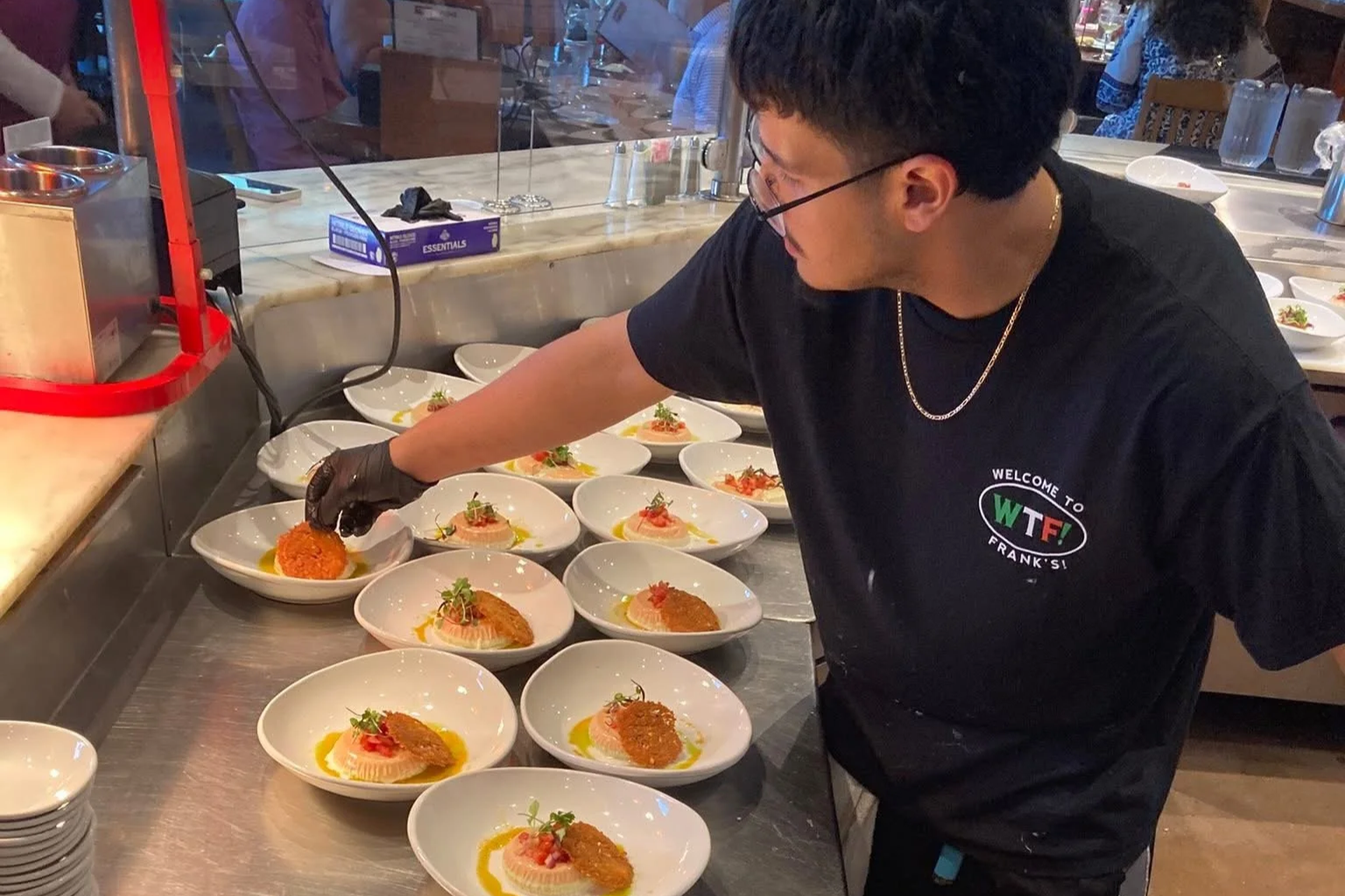 A chef arranging dishes with breaded appetizers and garnishes on white plates in a professional kitchen.