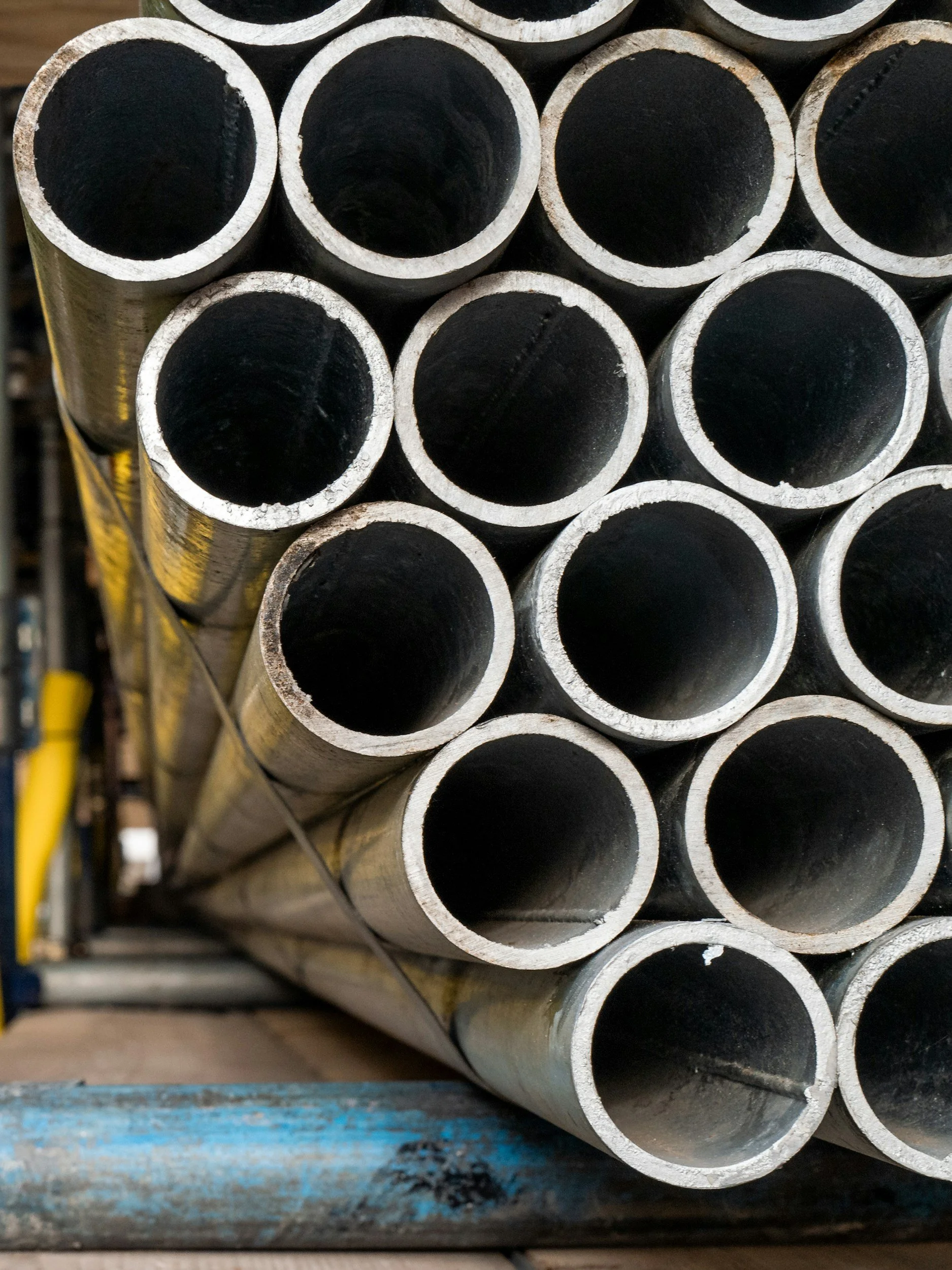 A stack of metal pipes with black insides, arranged horizontally on a blue wooden surface.