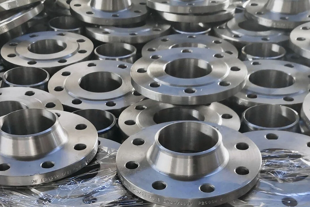 Multiple metal flanges stacked together in a manufacturing setting.