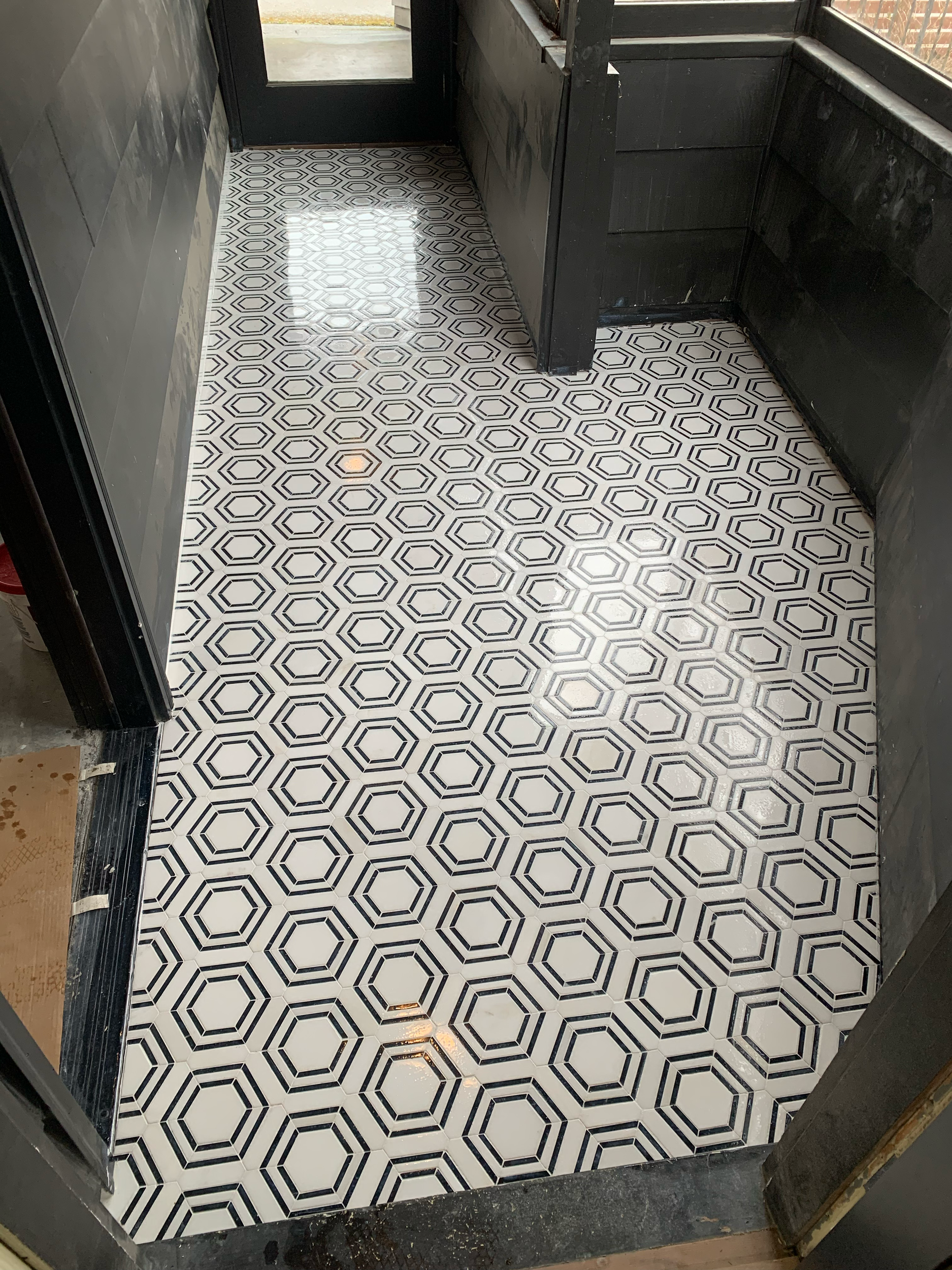 Black and white patterned tile floor at the entrance of a building, with black walls and a glass door in the background.