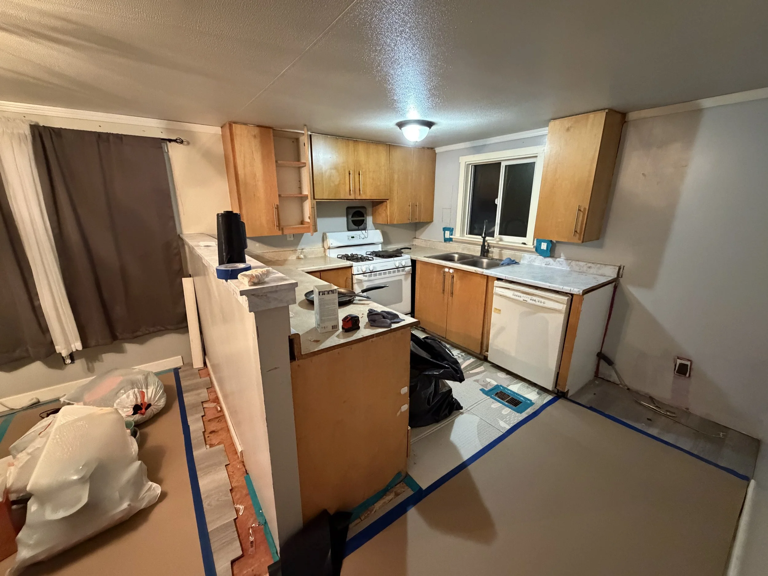 Kitchen under renovation with upper cabinets, a window above the sink, and construction supplies and tool on the counter and floor.