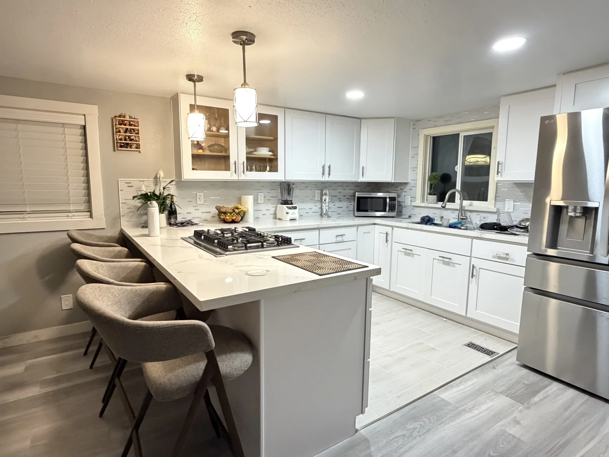 Modern kitchen with white cabinets, a kitchen island with bar stools, stainless steel appliances, and a window with a potted plant on the sill.