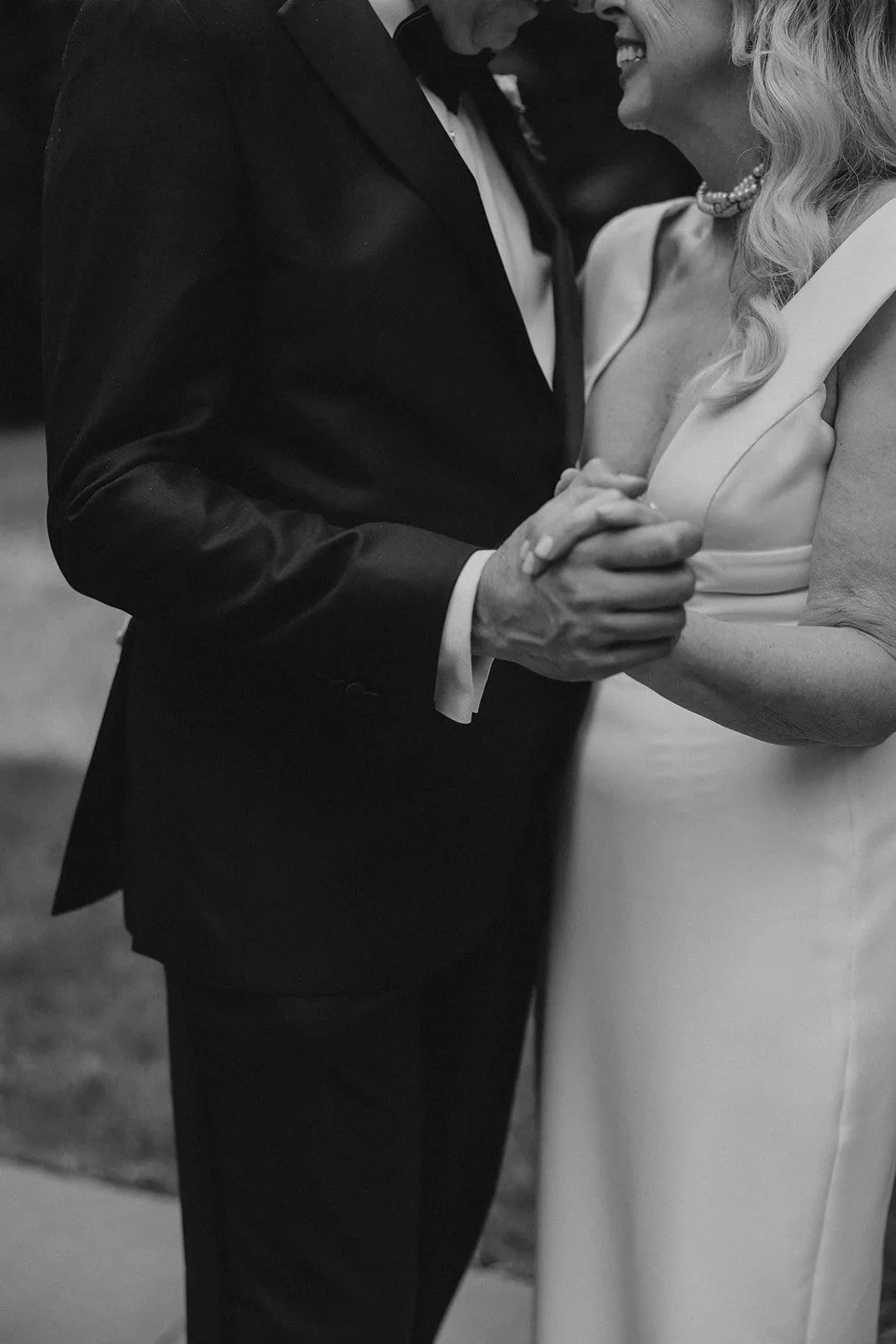 A black-and-white photo of a couple dancing closely, holding hands, with the woman smiling.