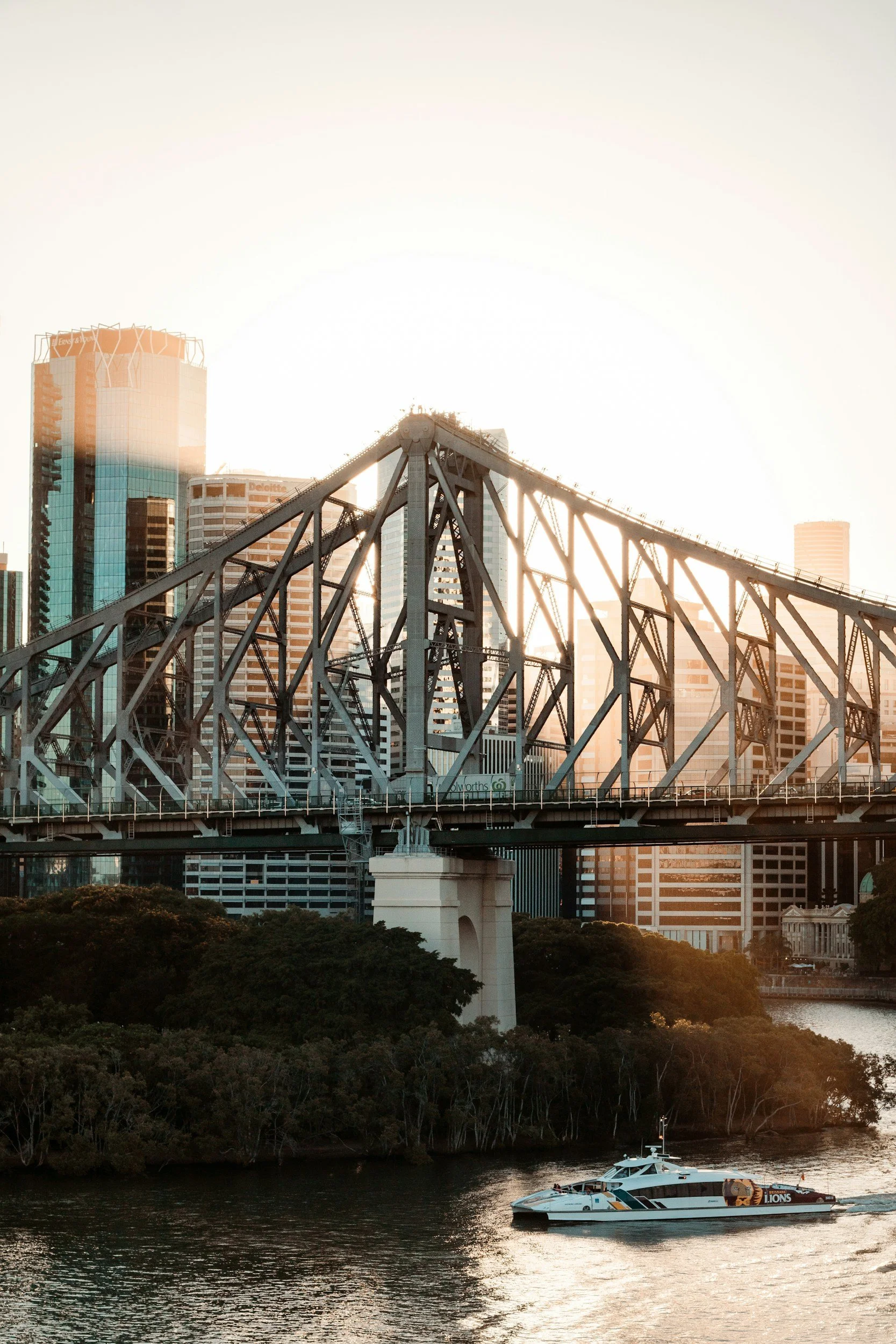 The photo shows a city skyline with tall modern buildings, a bridge, and a boat on the water at sunset.
