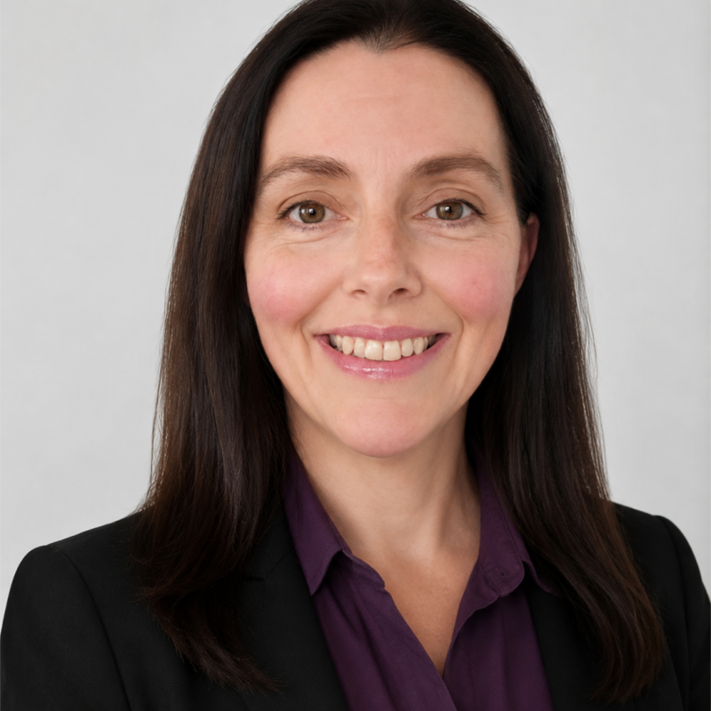 Professional woman with dark brown hair, wearing a black blazer and purple blouse, smiling against a neutral background.