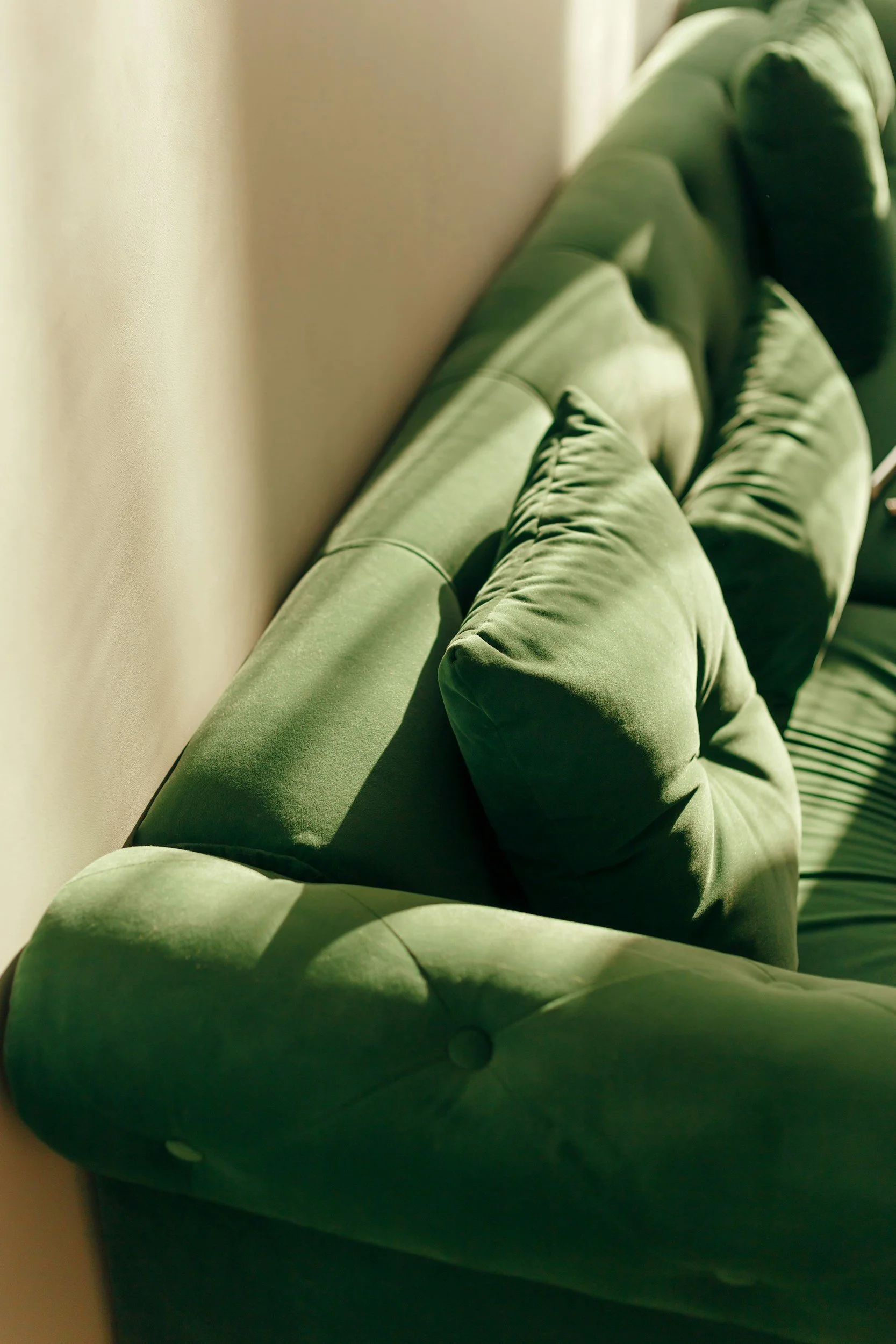 Green velvet tufted sofa next to a white wall.