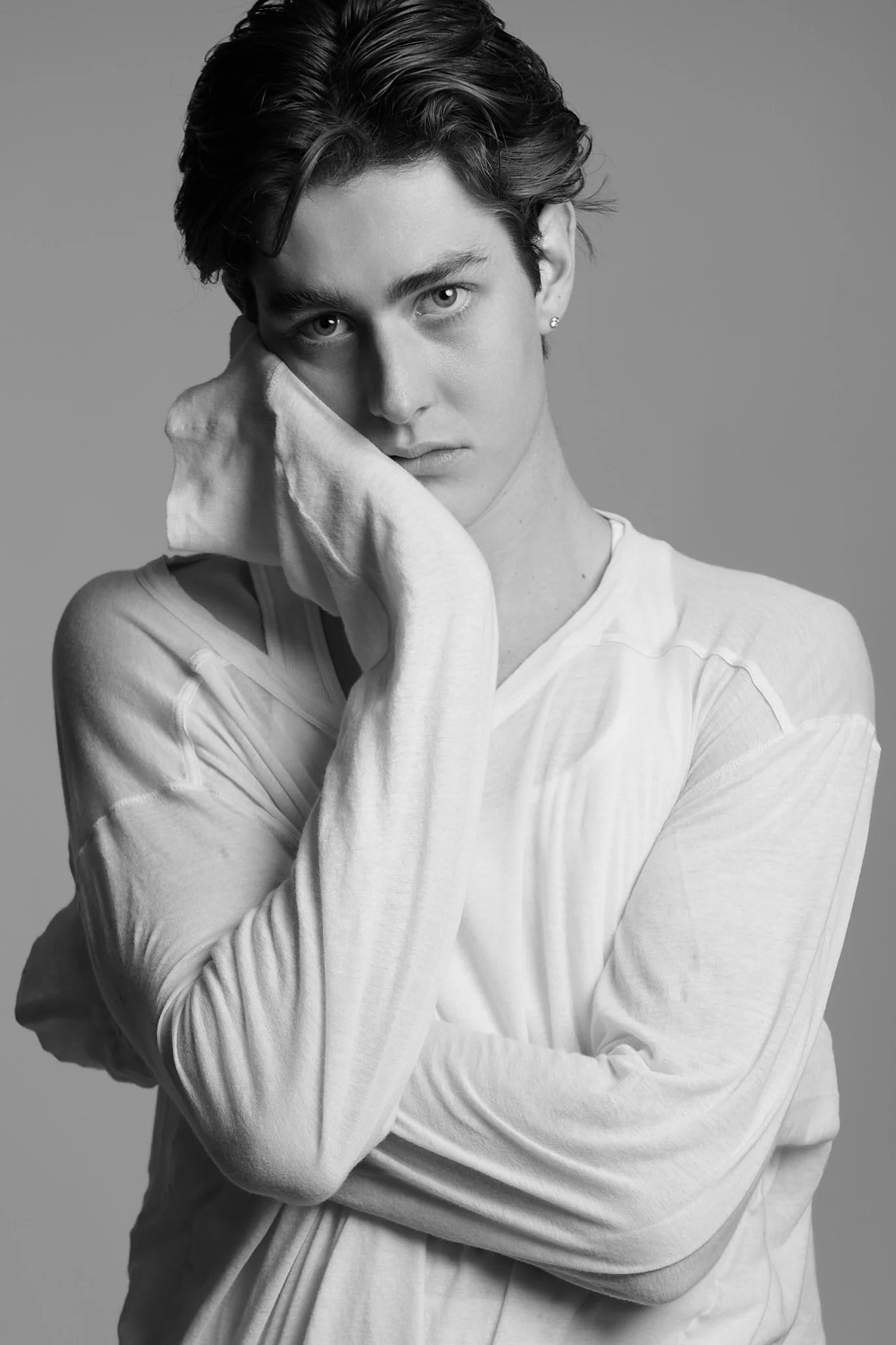 Black and white portrait of a young woman with short, dark hair, wearing a light-colored shirt, resting her chin on her hand with a serious expression, against a gray background.