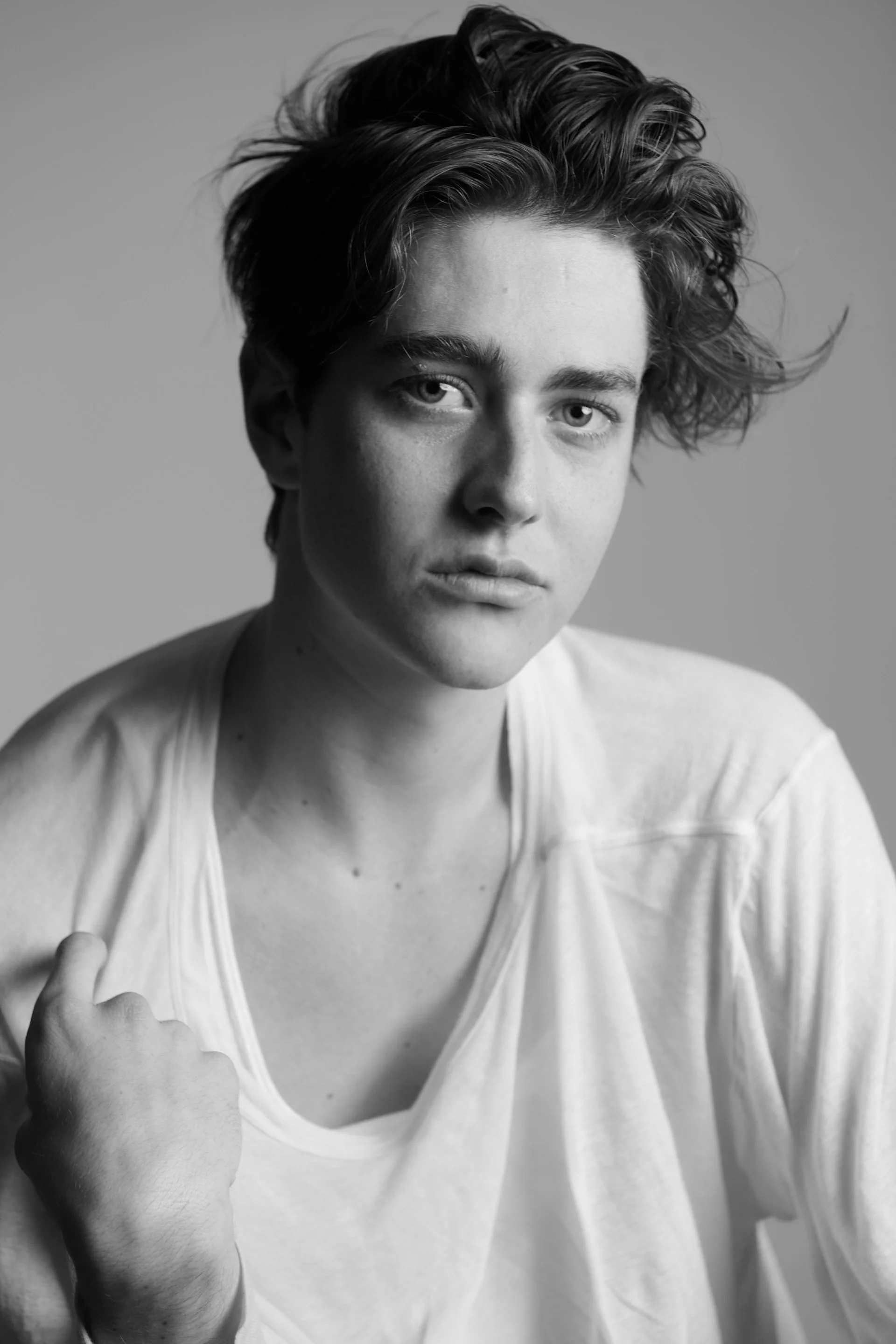 Black and white photo of a young man with messy hair, wearing a loose t-shirt, showing middle finger, with a serious expression.