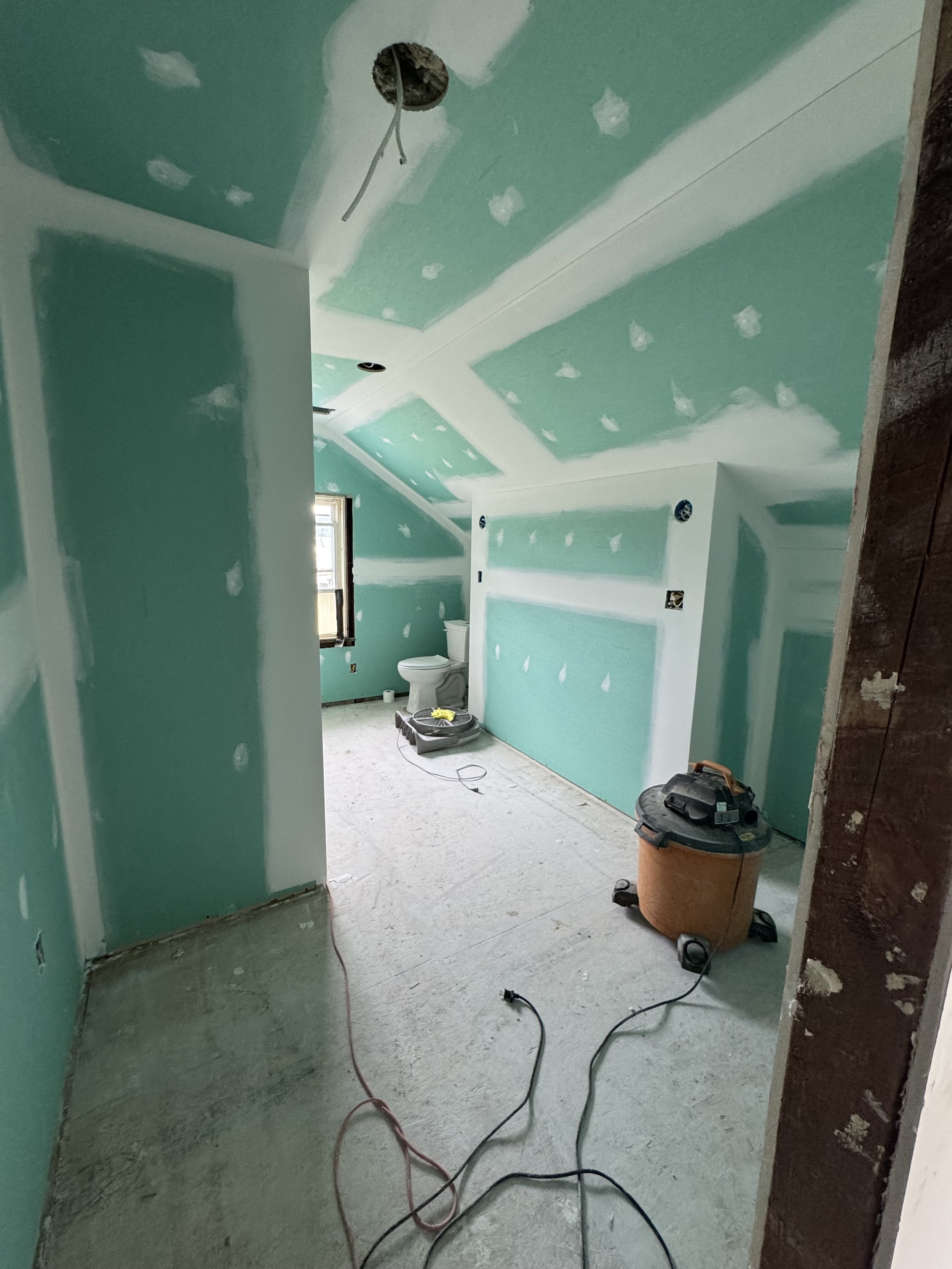 Interior of a room under construction with green drywall, unfinished walls, tools, and construction equipment.