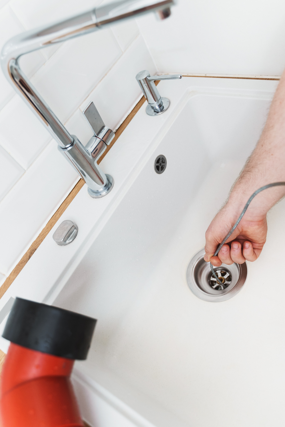 A person cleaning a kitchen sink drain with a flexible drain snake.