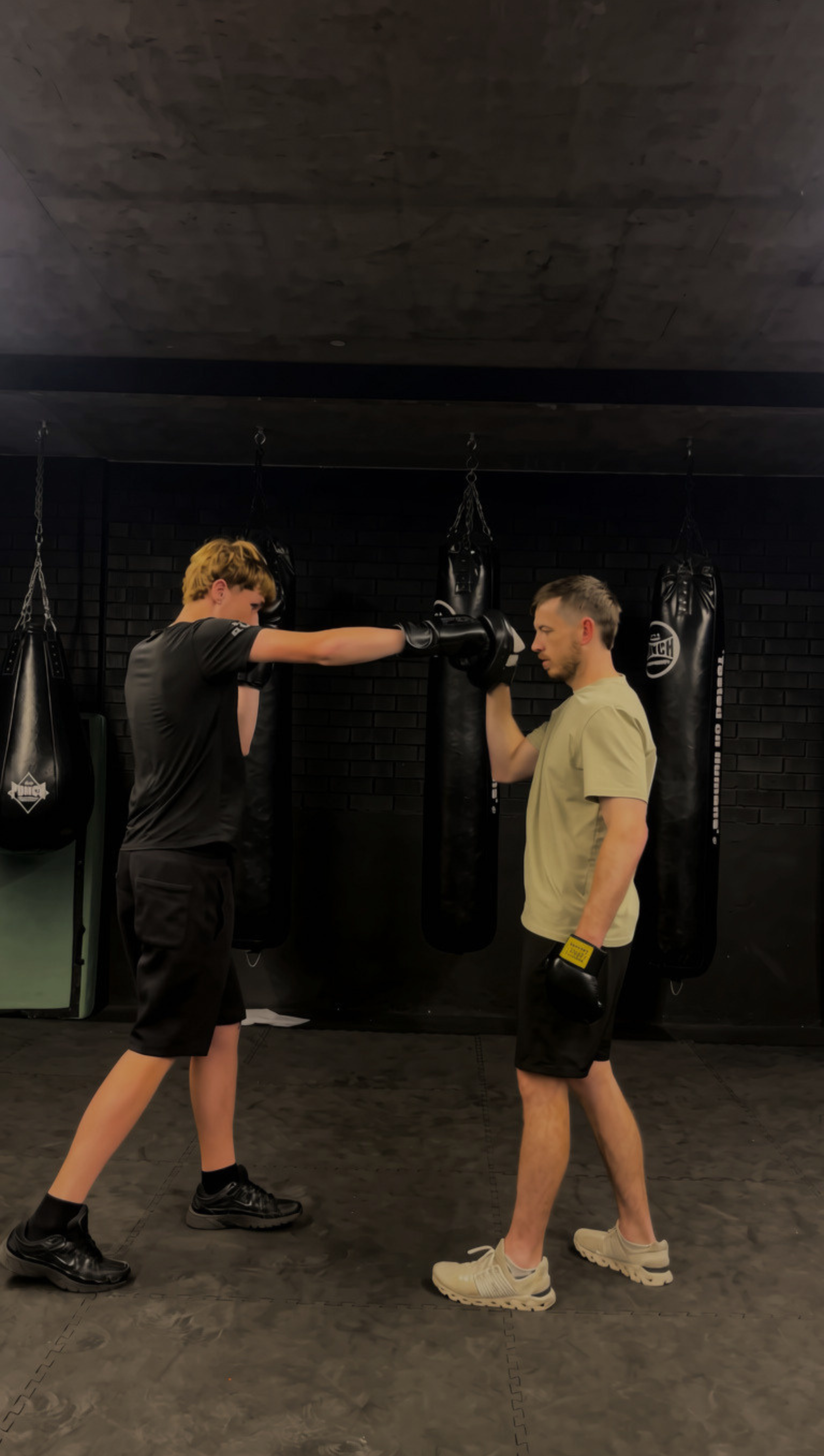 “Boxing coach Stuart guiding a teenage student through technique inside a gym, demonstrating proper form and offering supportive instruction.