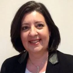 Portrait of a woman with dark hair smiling at the camera, wearing a black blazer and a white top.