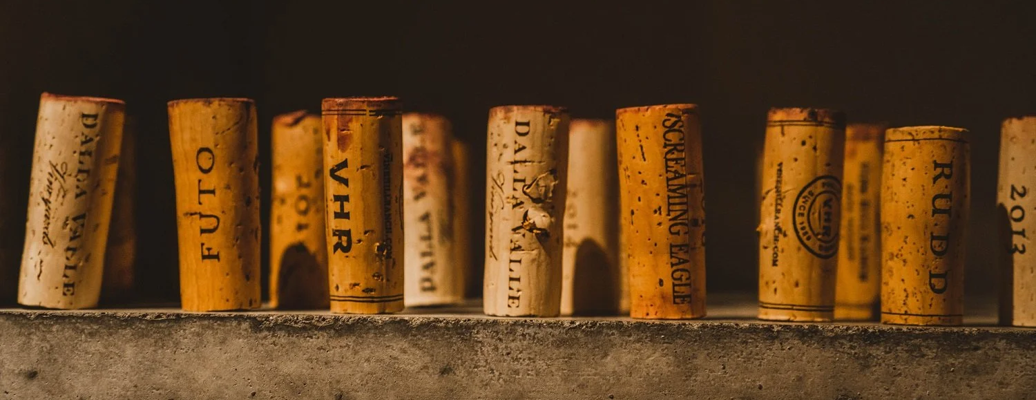 Close-up of used wine corks arranged in a row on a concrete surface, with a dark background.