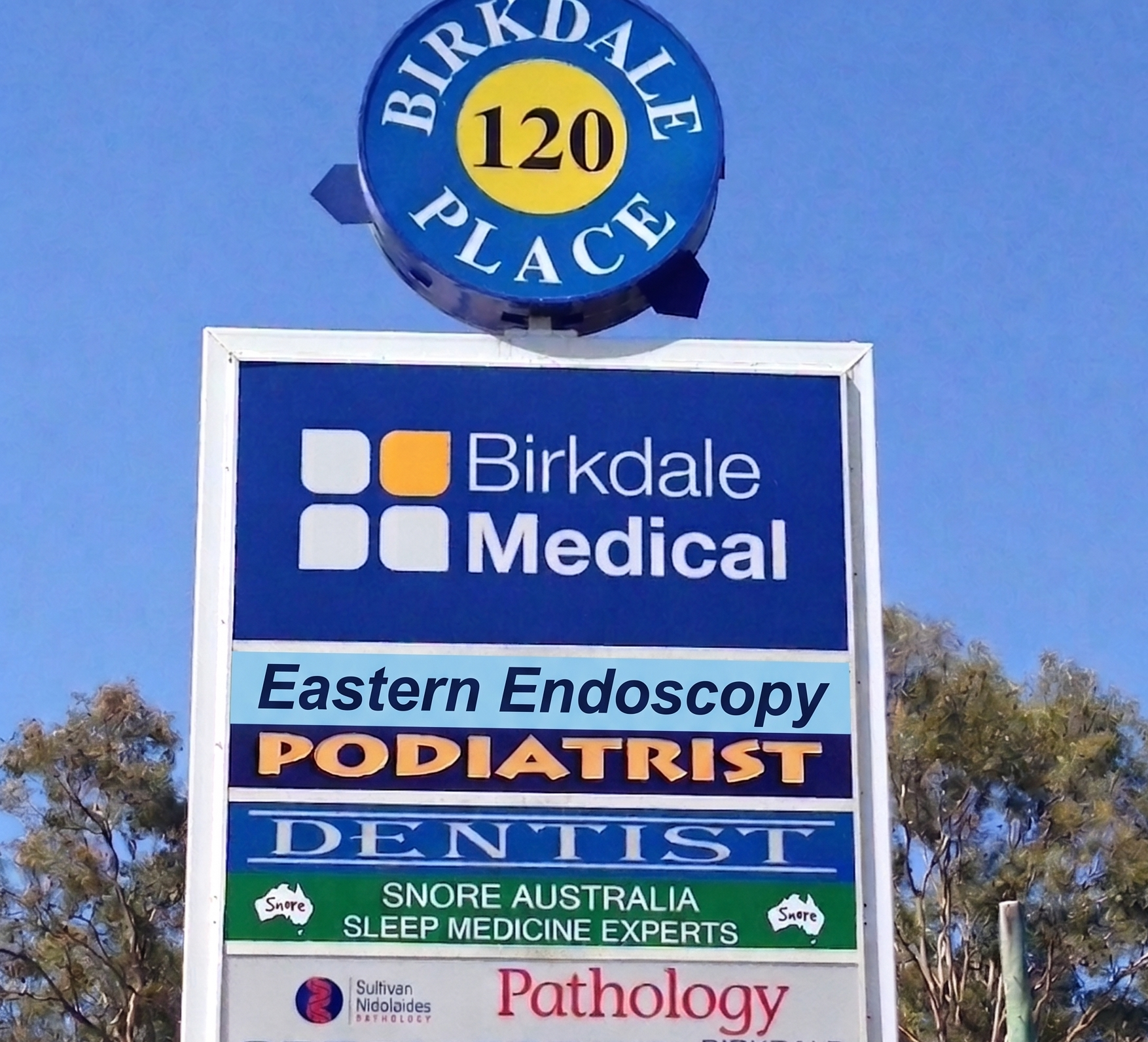 Sign for Birkdale Medical, showing services like Endoscopy, Podiatrist, Dentist, and Pathology along with Snore Australia sleep medicine experts, with trees in the background.