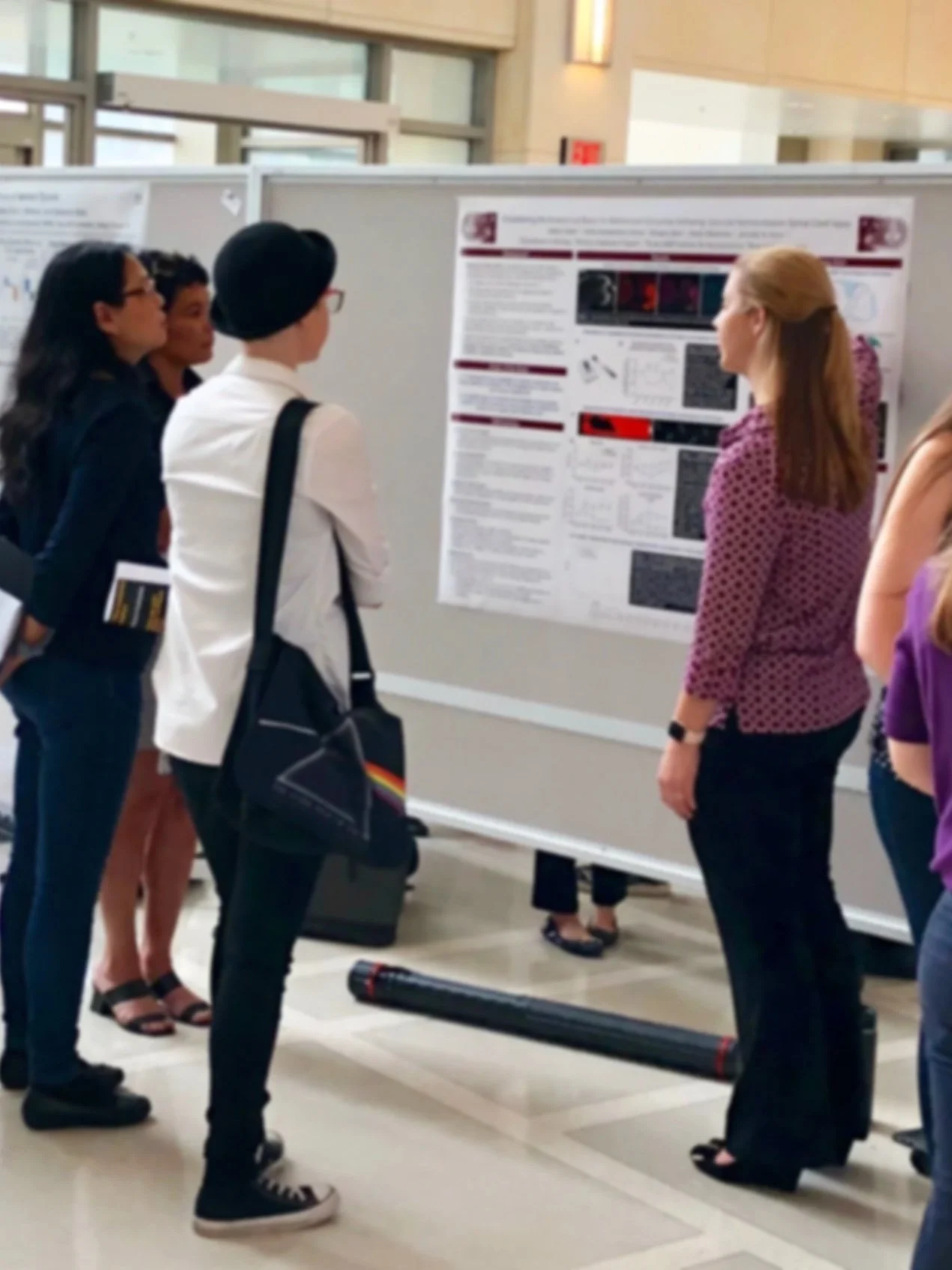 Group of people at a science or research poster presentation, looking at a large research poster on a display board.