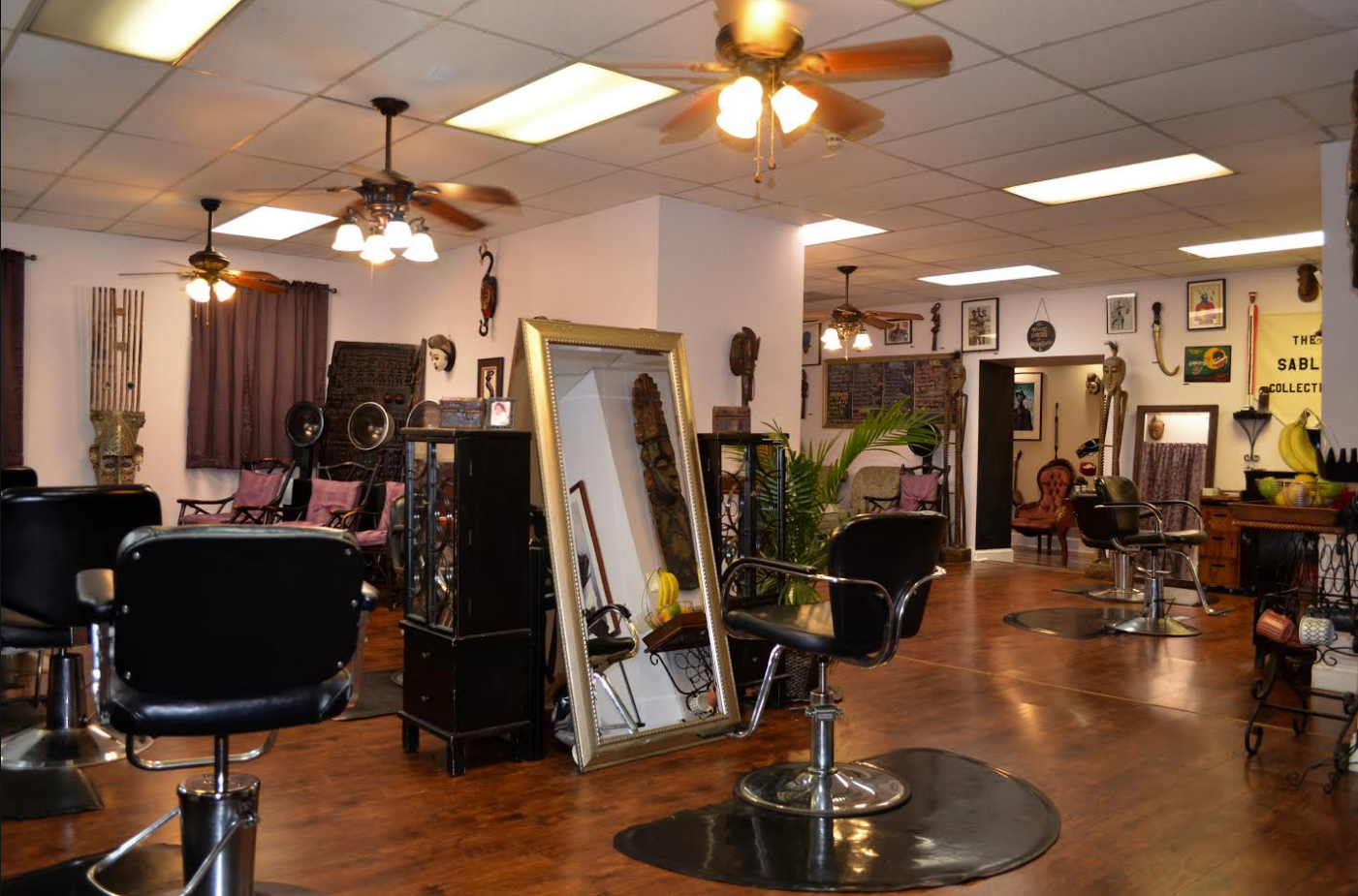 Interior of a vintage hair salon with styling chairs, mirrors, and decor, featuring wooden flooring and ceiling fans.