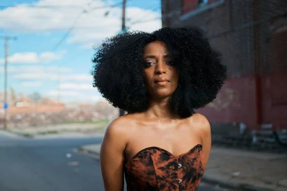 Woman with large curly hair walking outdoors in an urban area.