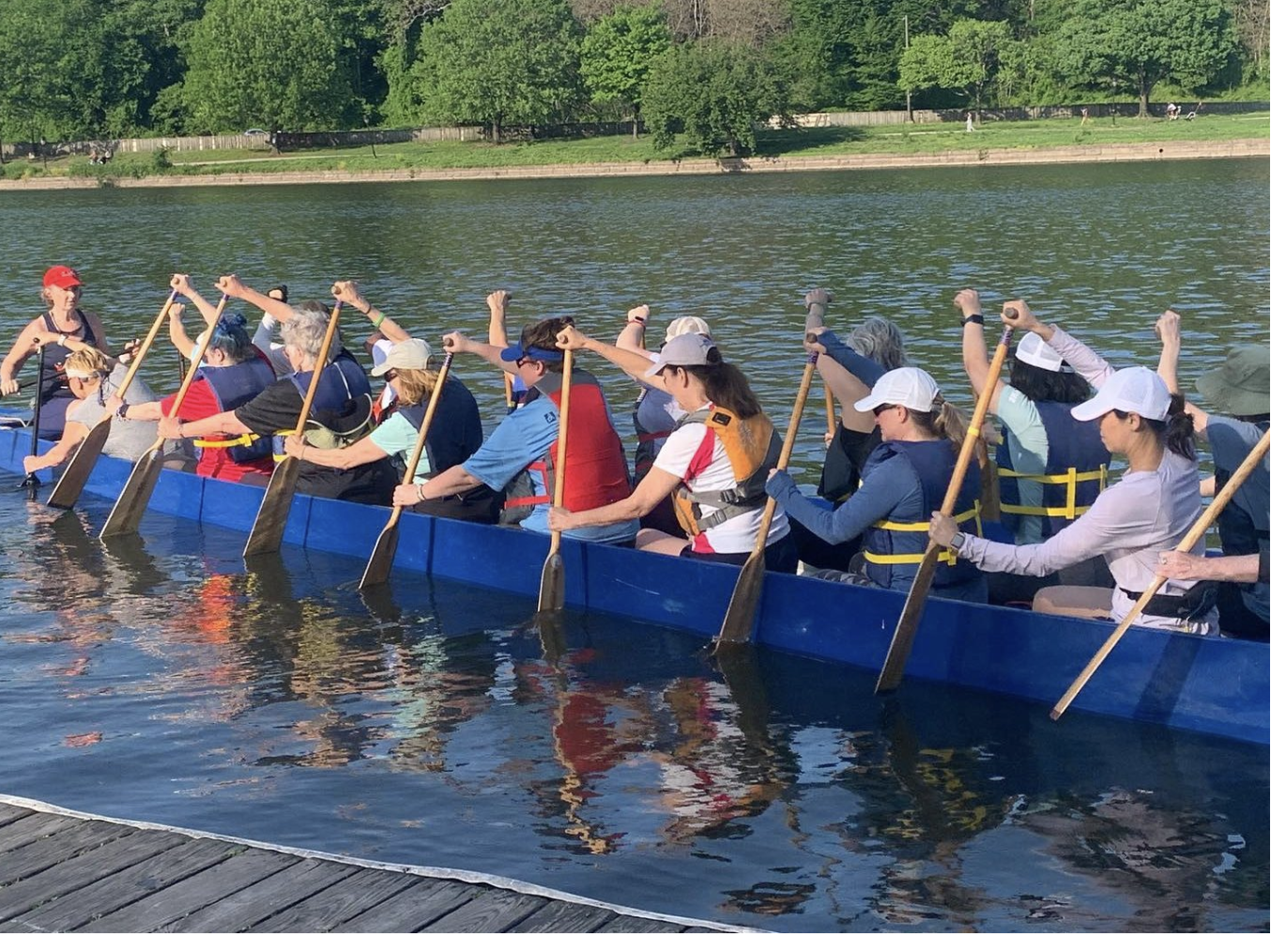 A group of people paddling a long blue dragon boat on a lake.