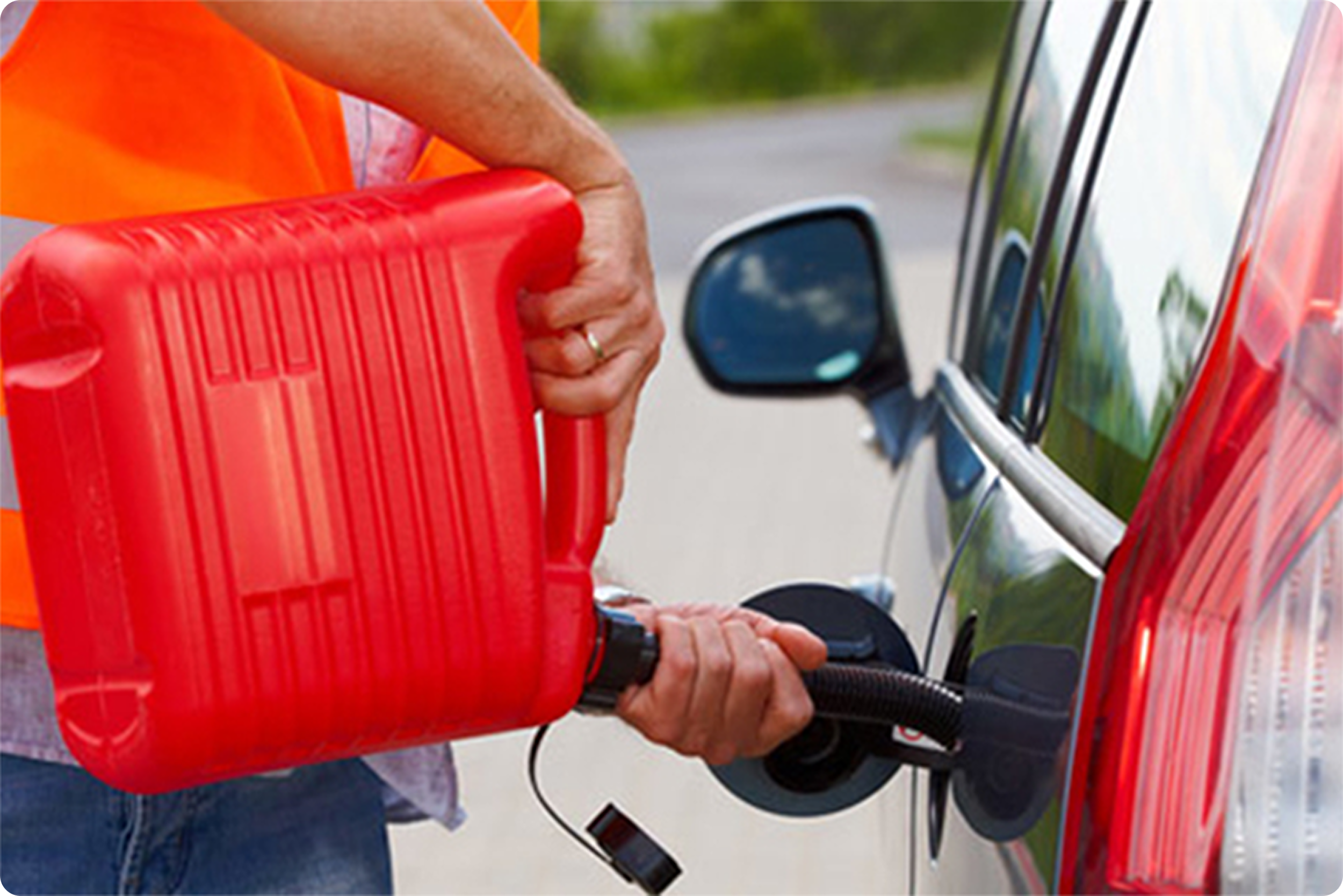 A person in an orange safety vest is refilling a red gasoline container from a gas pump nozzle while standing next to a red vehicle.