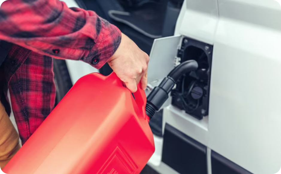 A person refueling a white vehicle with a red gas canister at a gas station.