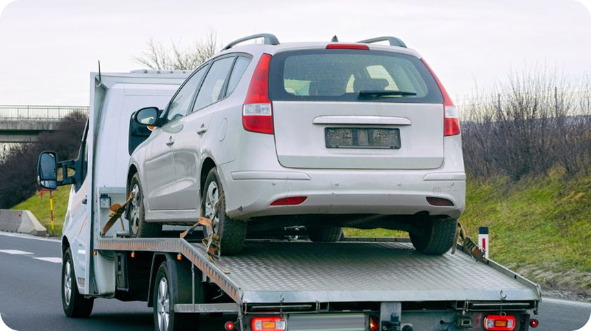 A white station wagon loaded onto a flatbed tow truck on the side of a highway.