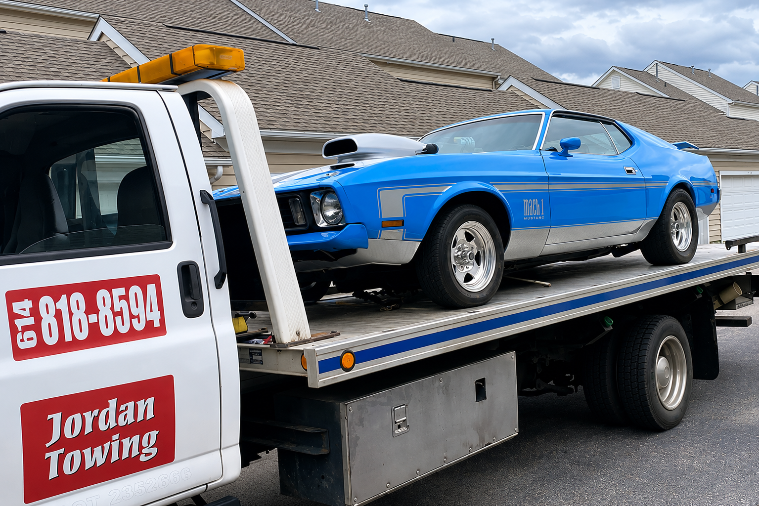 Blue vintage Ford Mustang Mach 1 being transported on a flatbed tow truck in a suburban neighborhood.