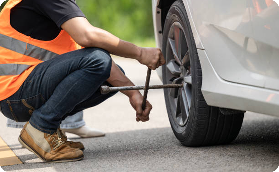 Person changing a car tire on the roadside.