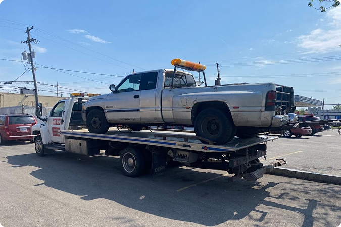 A work truck being towed on a flatbed tow truck in a parking lot under a partly cloudy sky.